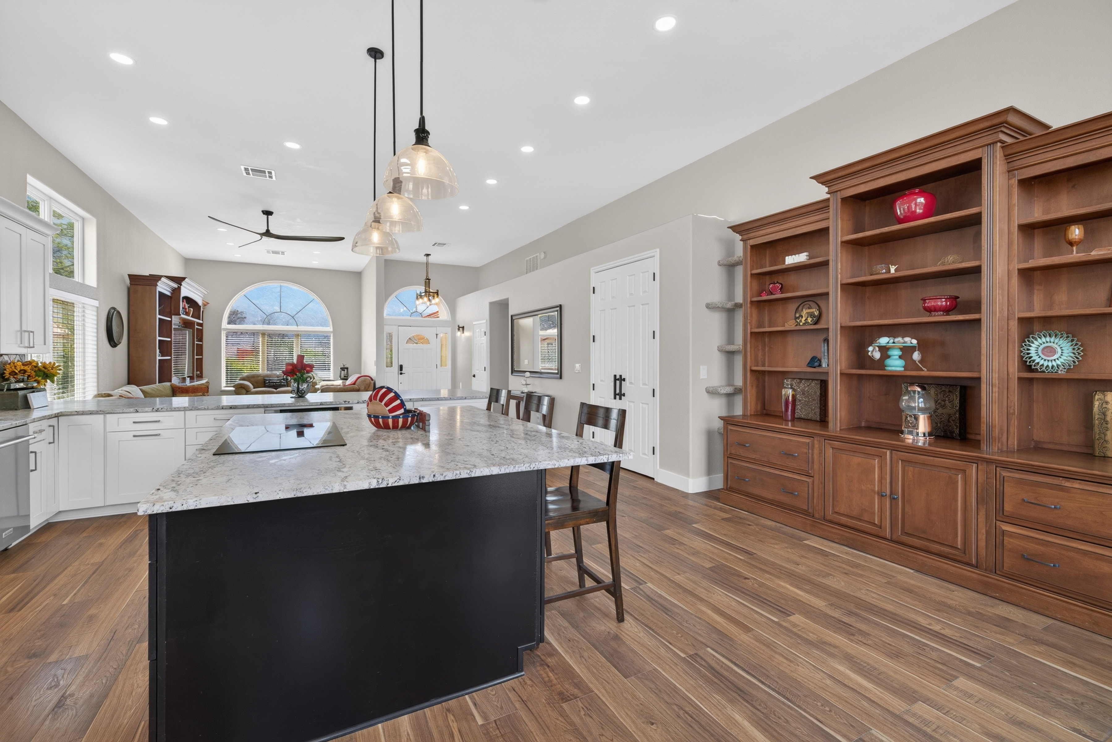 Spacious kitchen featuring a large island with an integrated cooktop, white perimeter cabinetry, pendant lighting, and wood-finish flooring