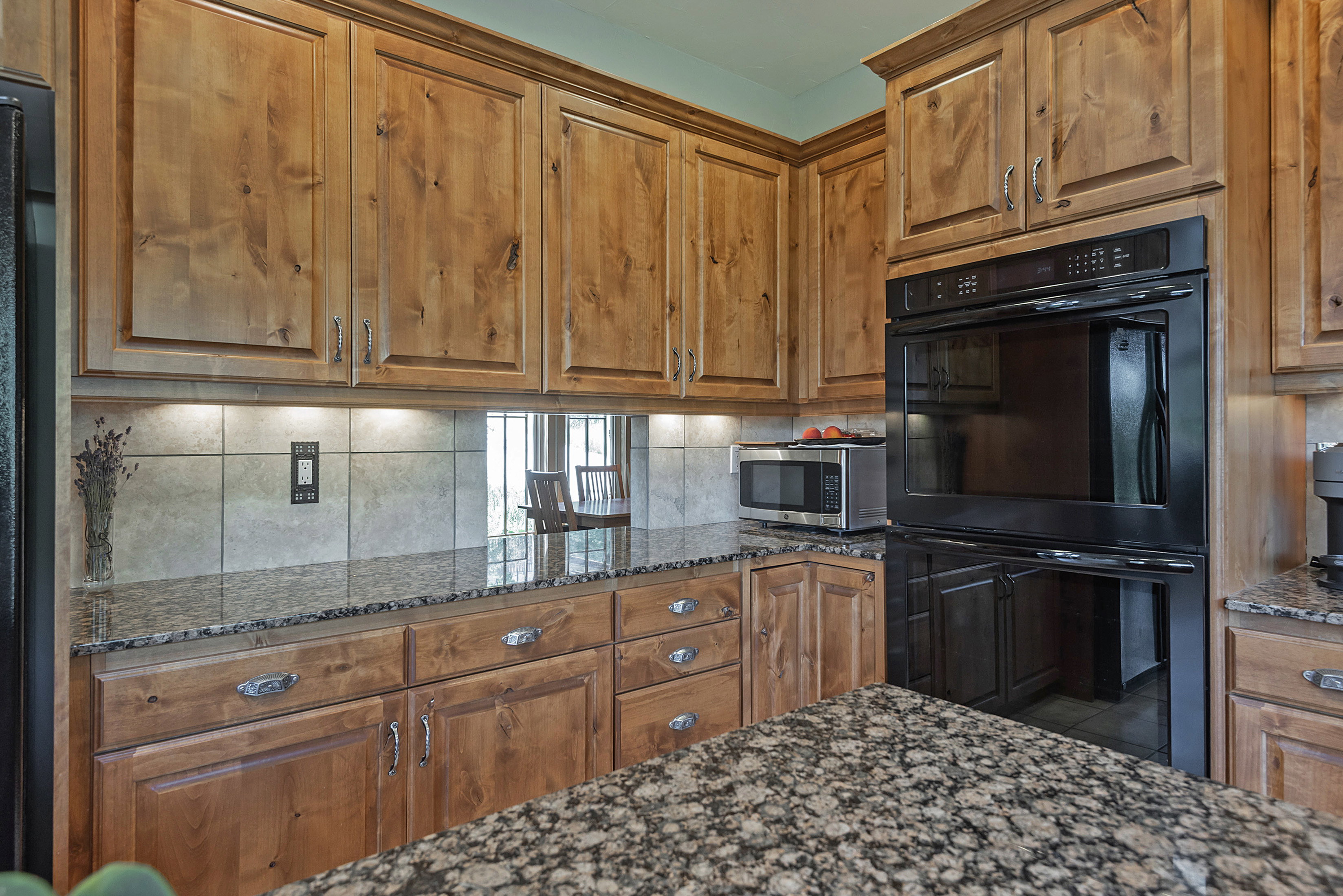 Built-in double oven within a kitchen featuring wood cabinetry, granite countertops, and a tiled backsplash