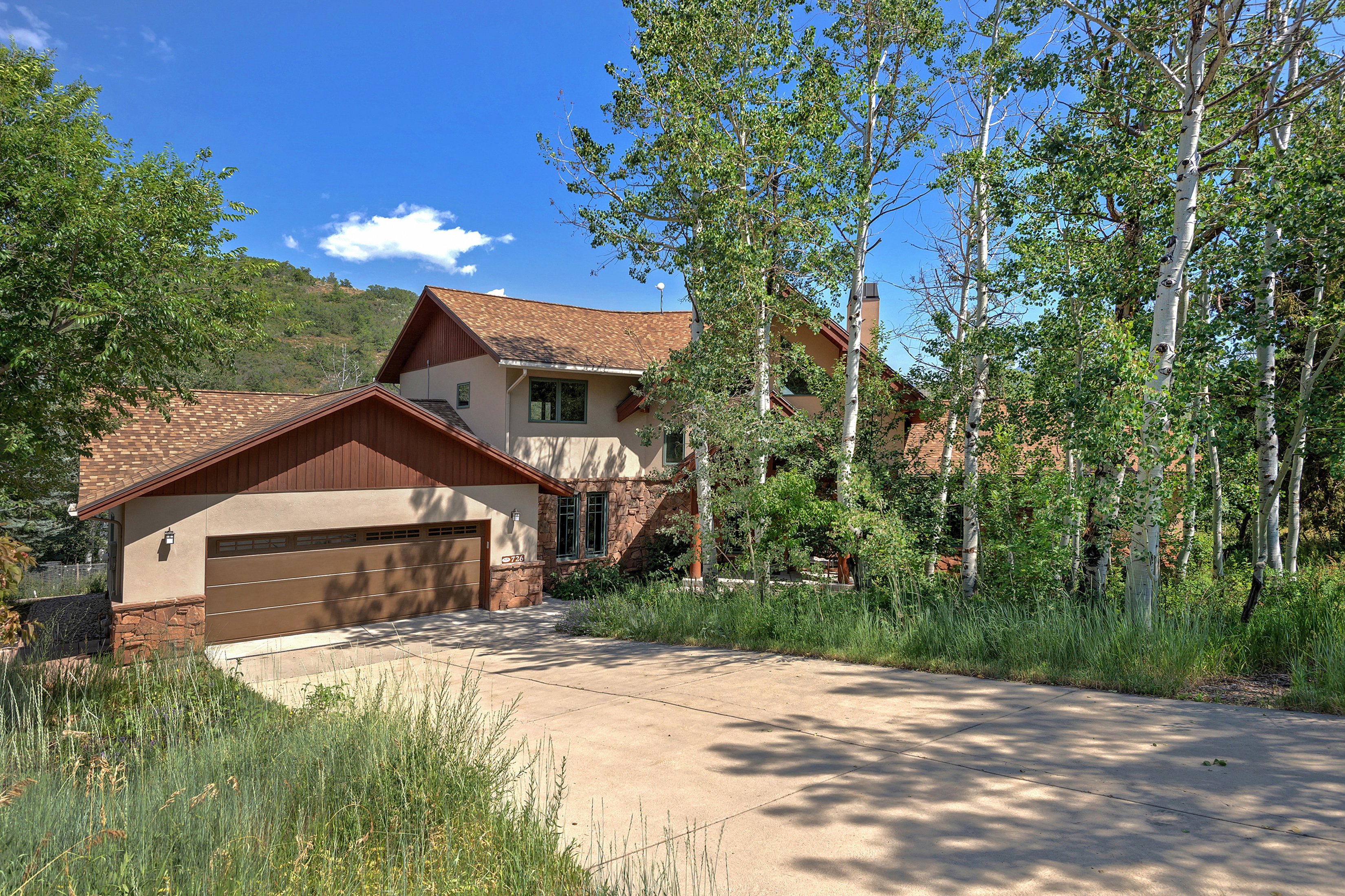 Multi-level residence featuring a two-car garage with a brown panel door, stone base detailing, and stucco siding