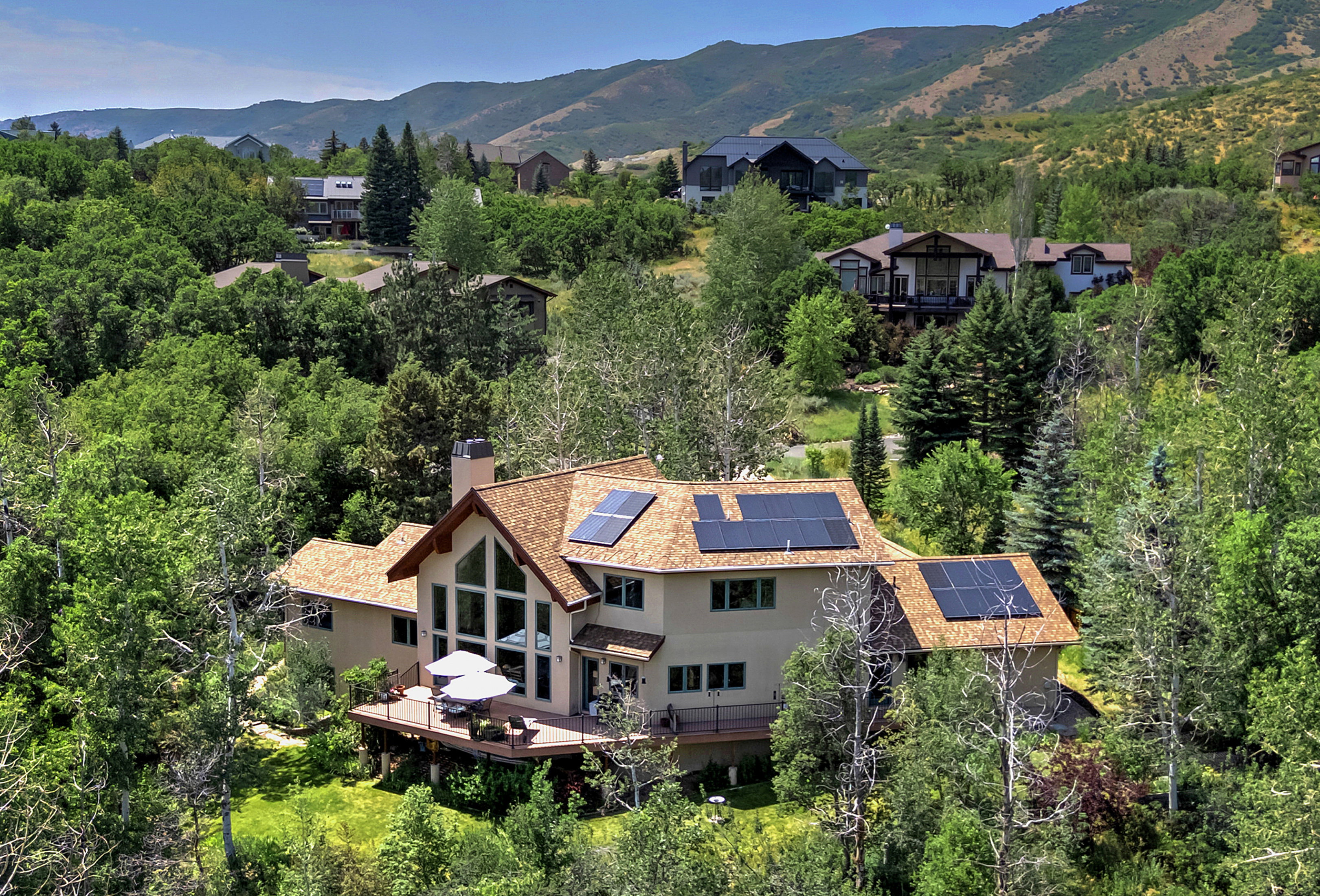 Contemporary residence featuring a prominent gabled roofline with integrated solar panels, a multi-level wood deck, and an expansive window wall