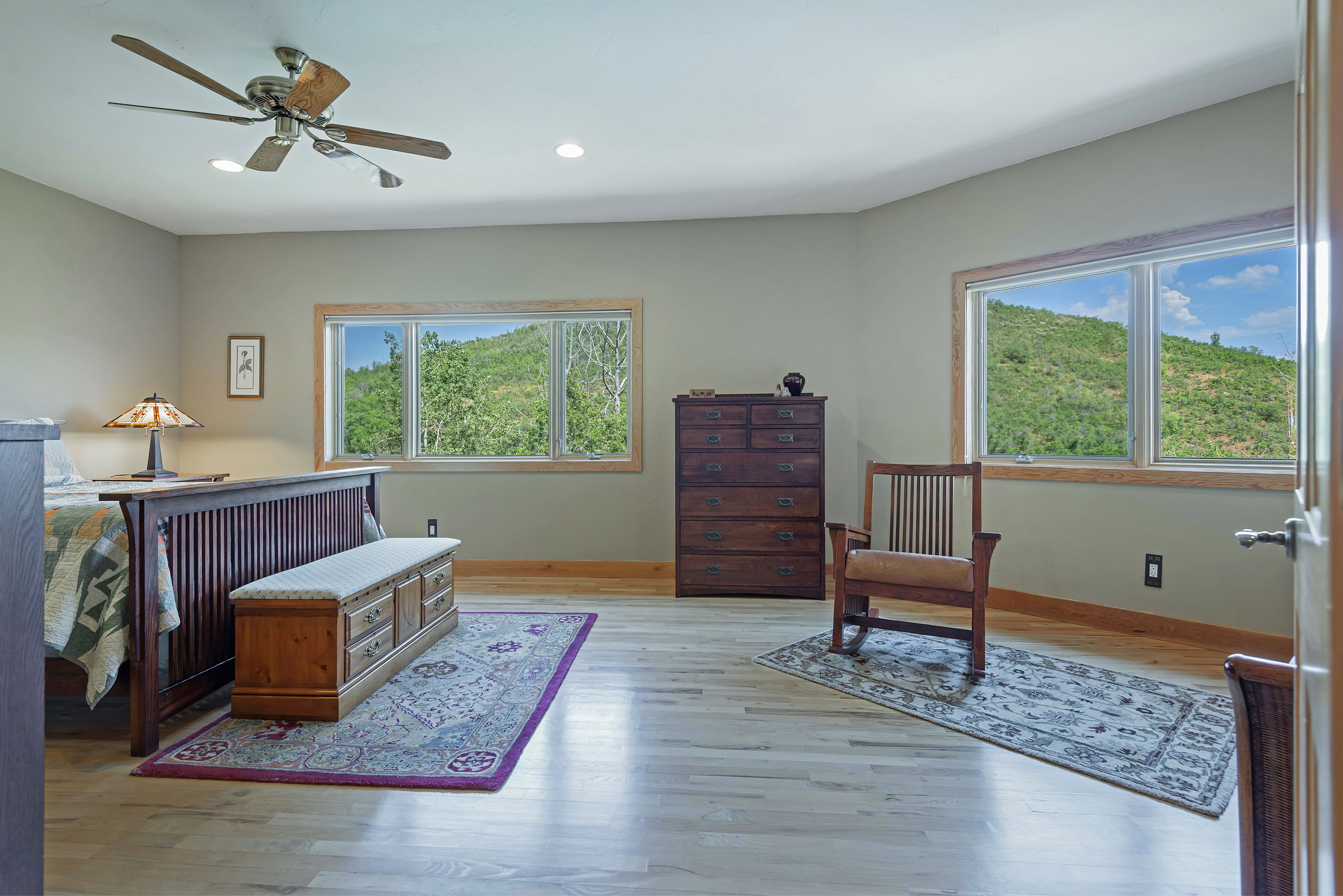 Spacious room with light wood-finish flooring, two large windows with natural wood trim, and a ceiling fan with integrated lighting