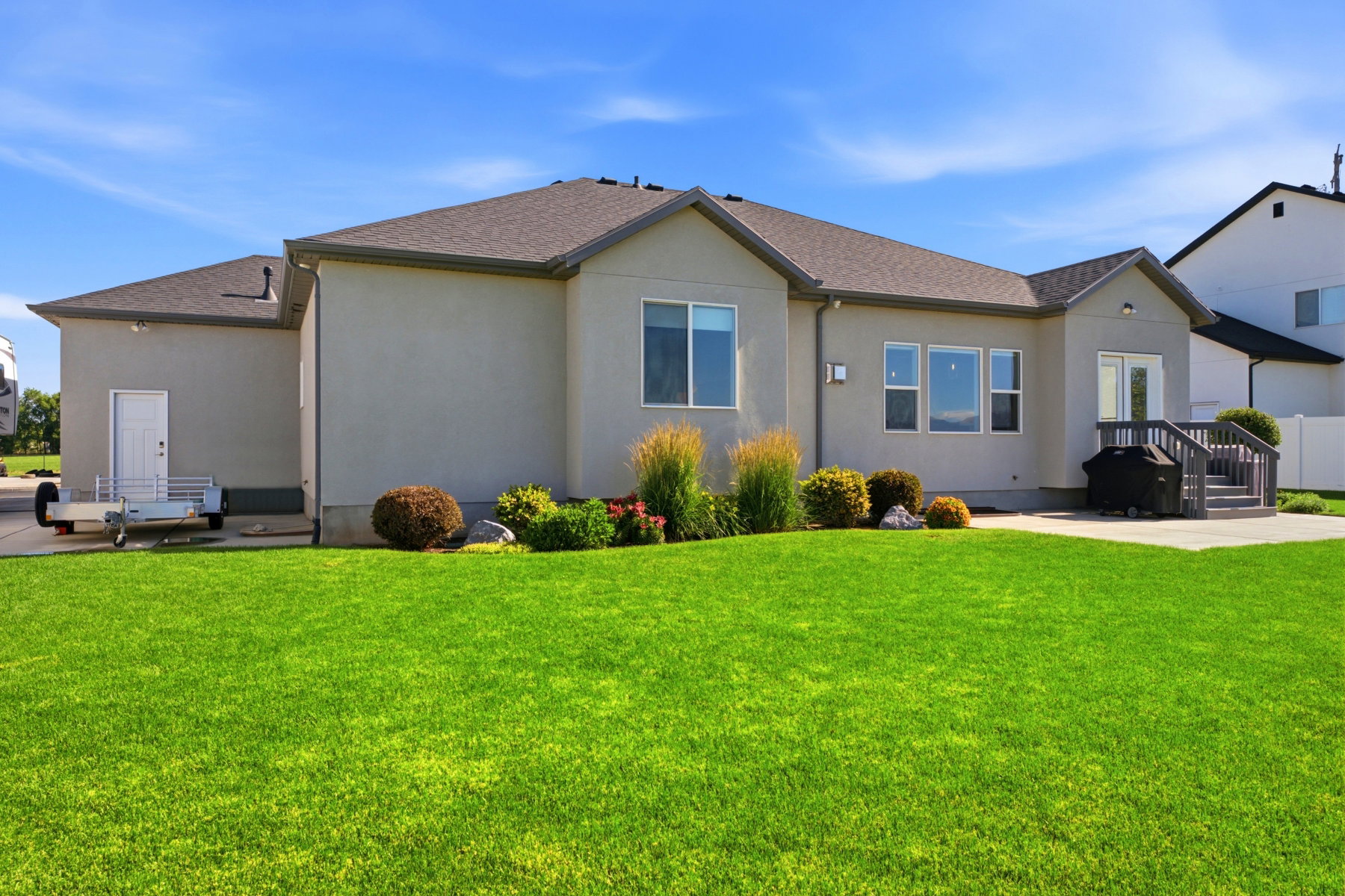 Expansive backyard featuring a lush lawn, concrete patio, and a wooden deck with railing