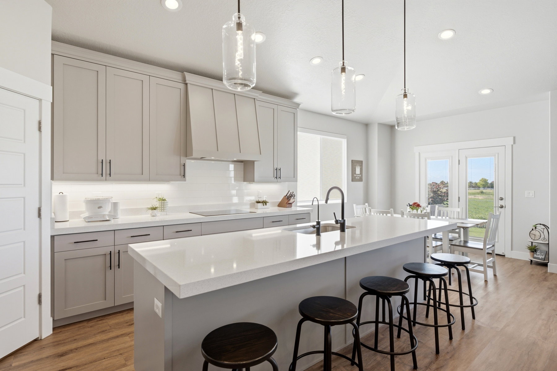 Spacious kitchen featuring an extended island with a built-in sink, light gray cabinetry, Quartz countertops, so much light and bar with seating