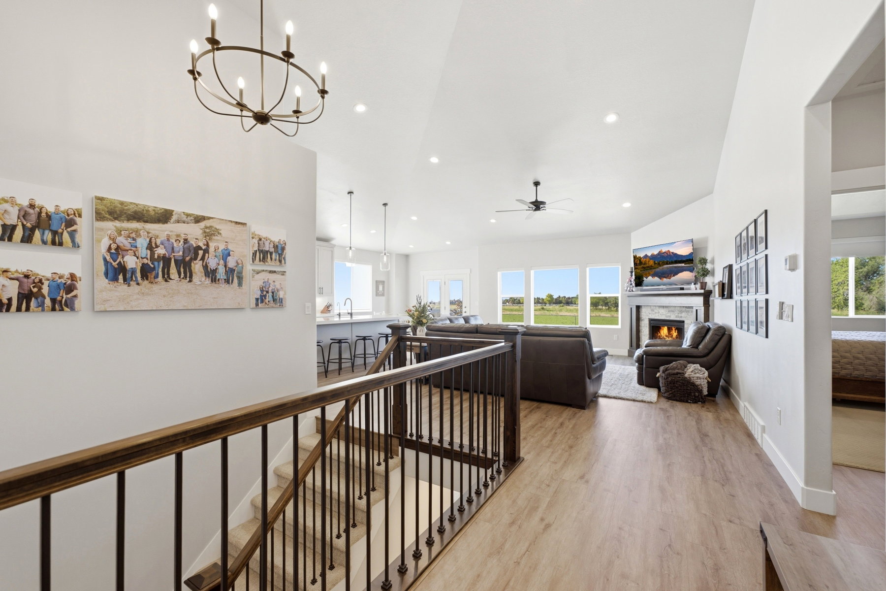 Open-concept living space featuring vaulted ceilings, wood-finish flooring, a fireplace with a stone surround and wood mantle, so many windows providing abundant natural light