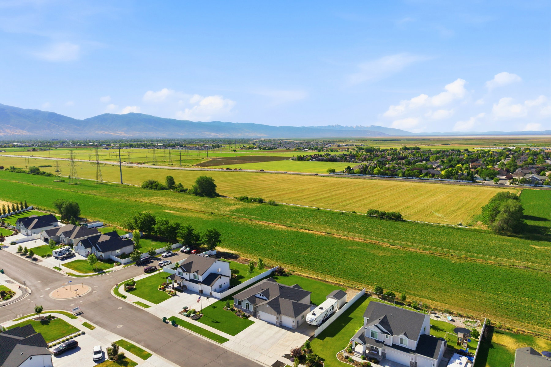 Aerial perspective featuring a residential street with cul-de-sac, surrounded by expansive green fields and distant mountains