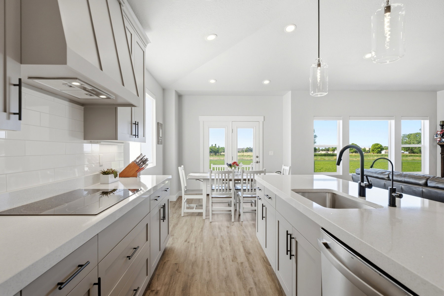 Modern kitchen featuring an expansive island with an undermount sink and matte black faucet, light wood-finish flooring, white subway tile backsplash, and stainless steel appliances