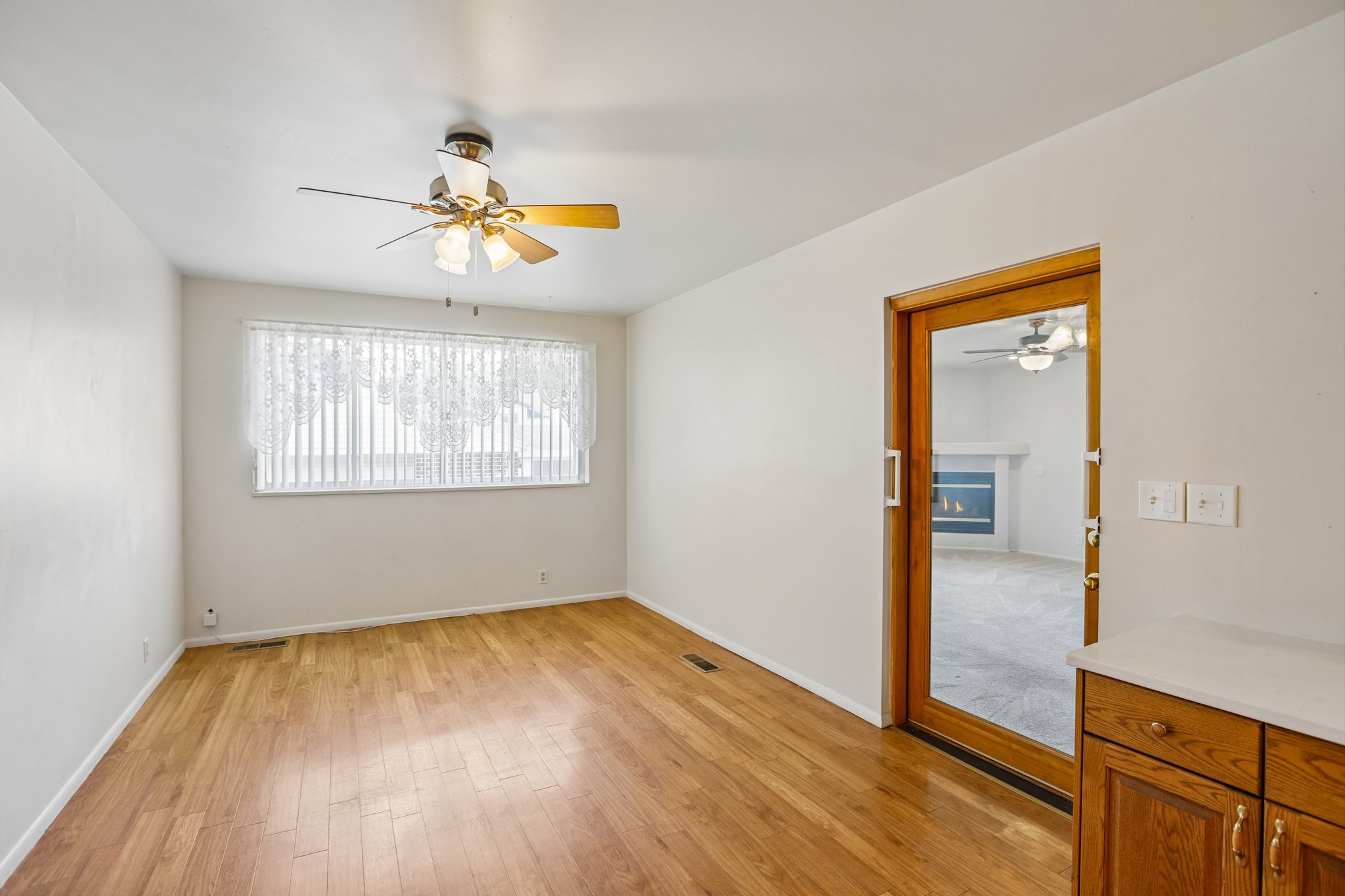 Room featuring wood-finish flooring, a ceiling fan with integrated lighting, and a large window with vertical blinds