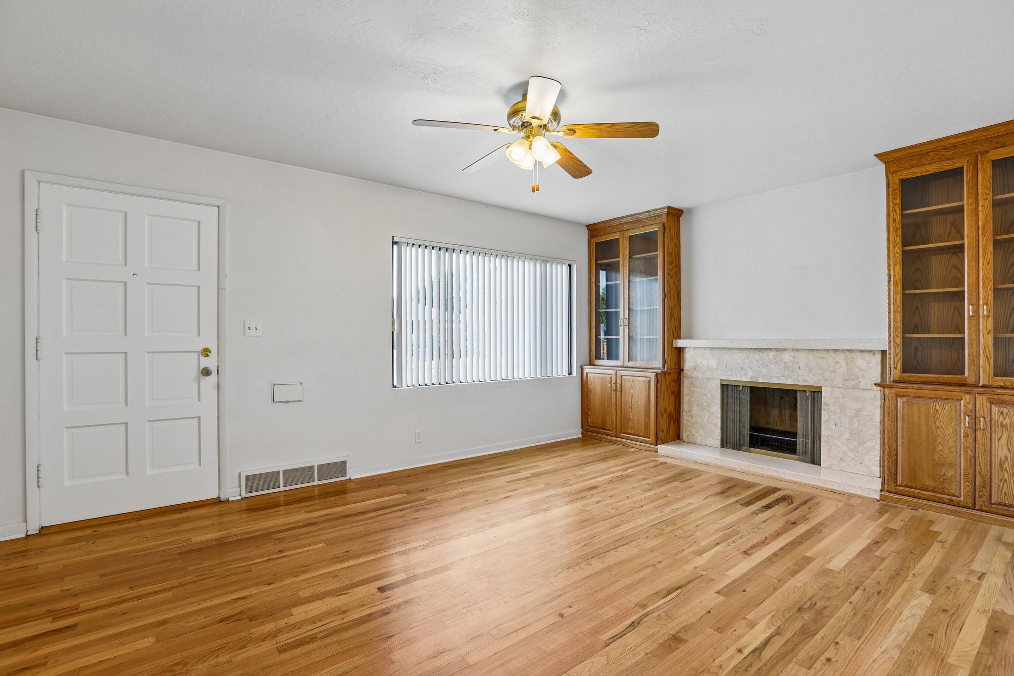Bright living area featuring wood-finish flooring, a ceiling fan, and a fireplace with a stone surround