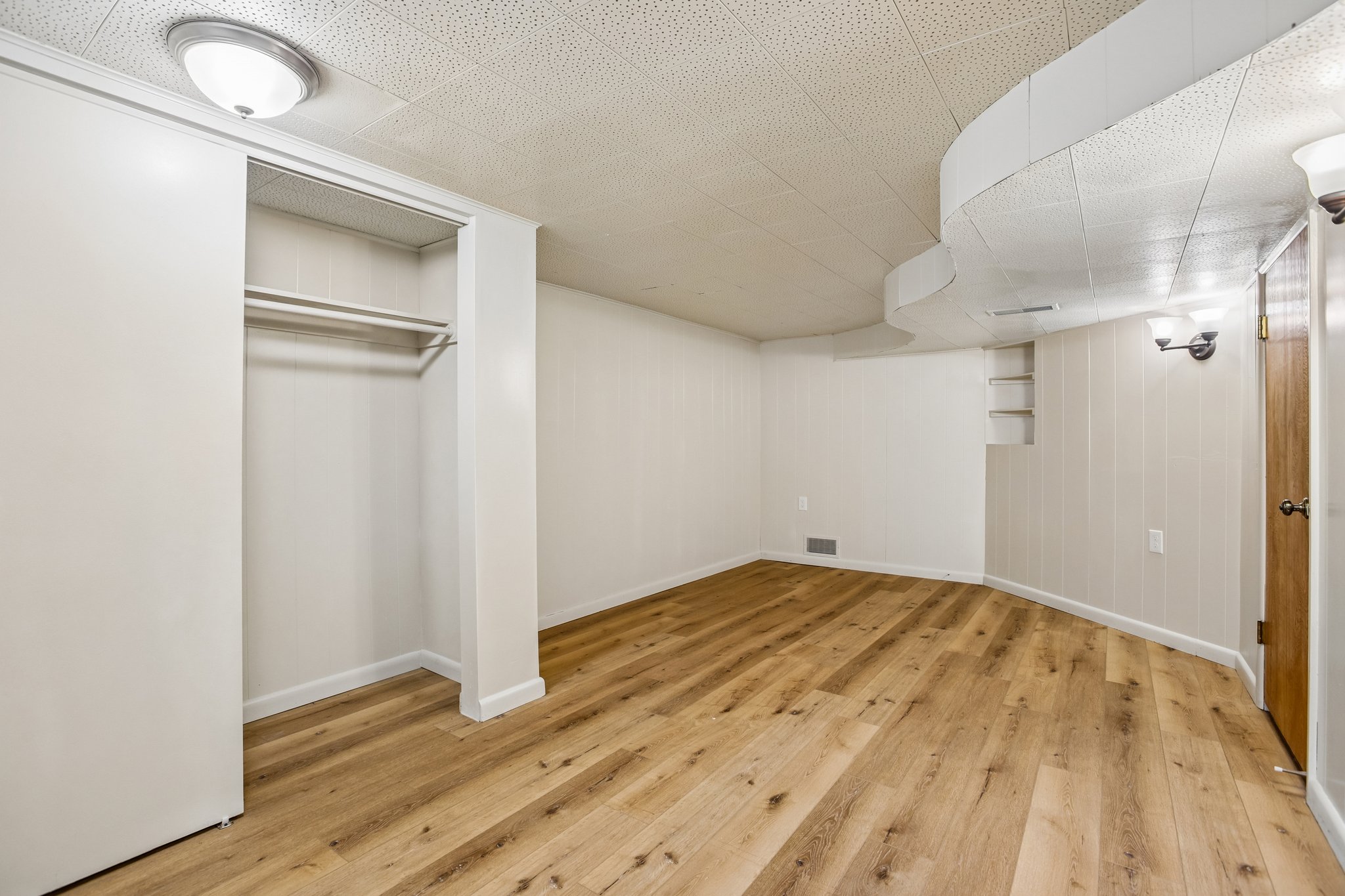 Room featuring wood-finish flooring, white paneled walls, and a recessed closet with dual rods