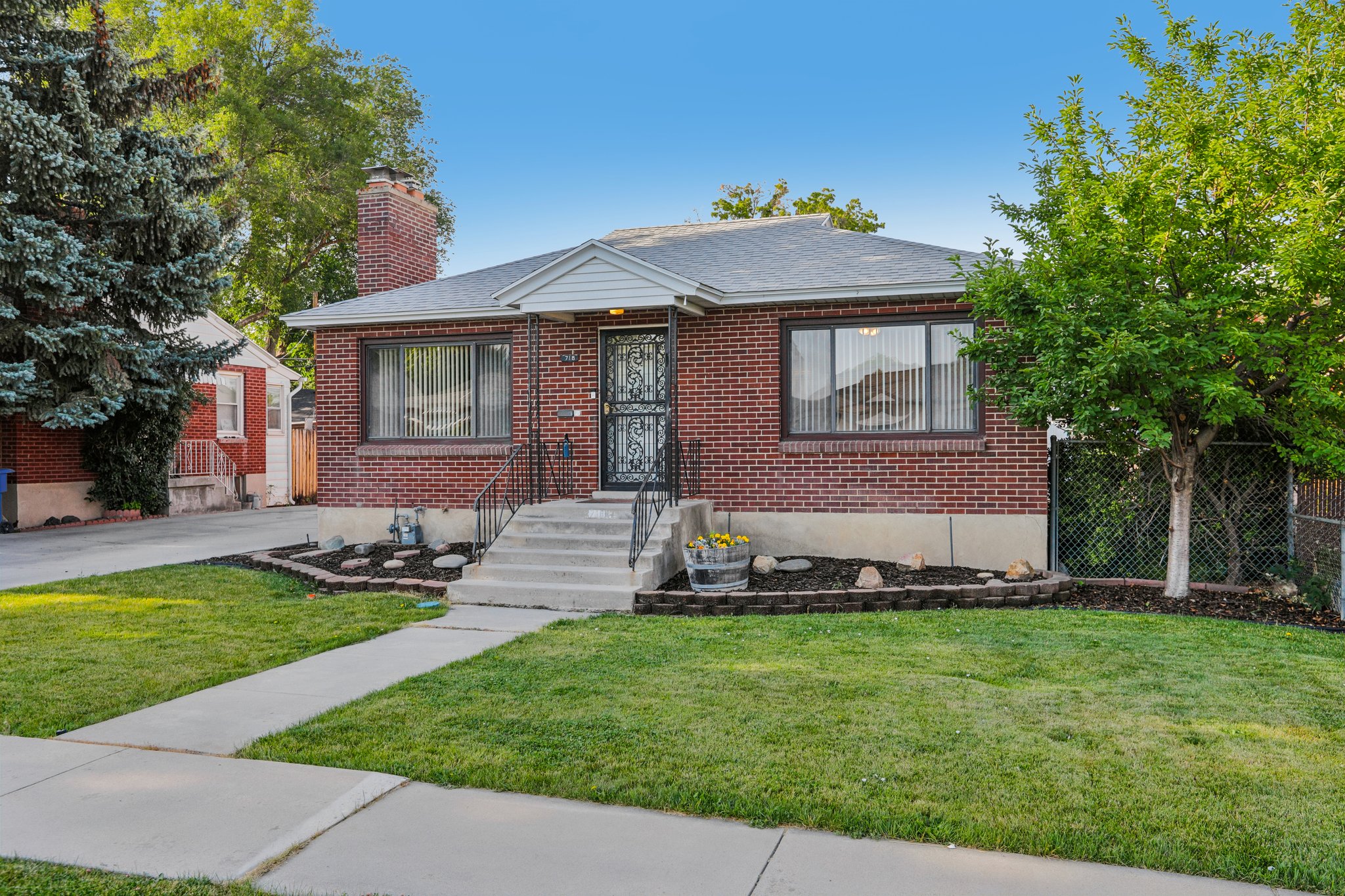 Brick residence with a prominent front entrance, featuring a concrete walkway, established front lawn, and mature trees