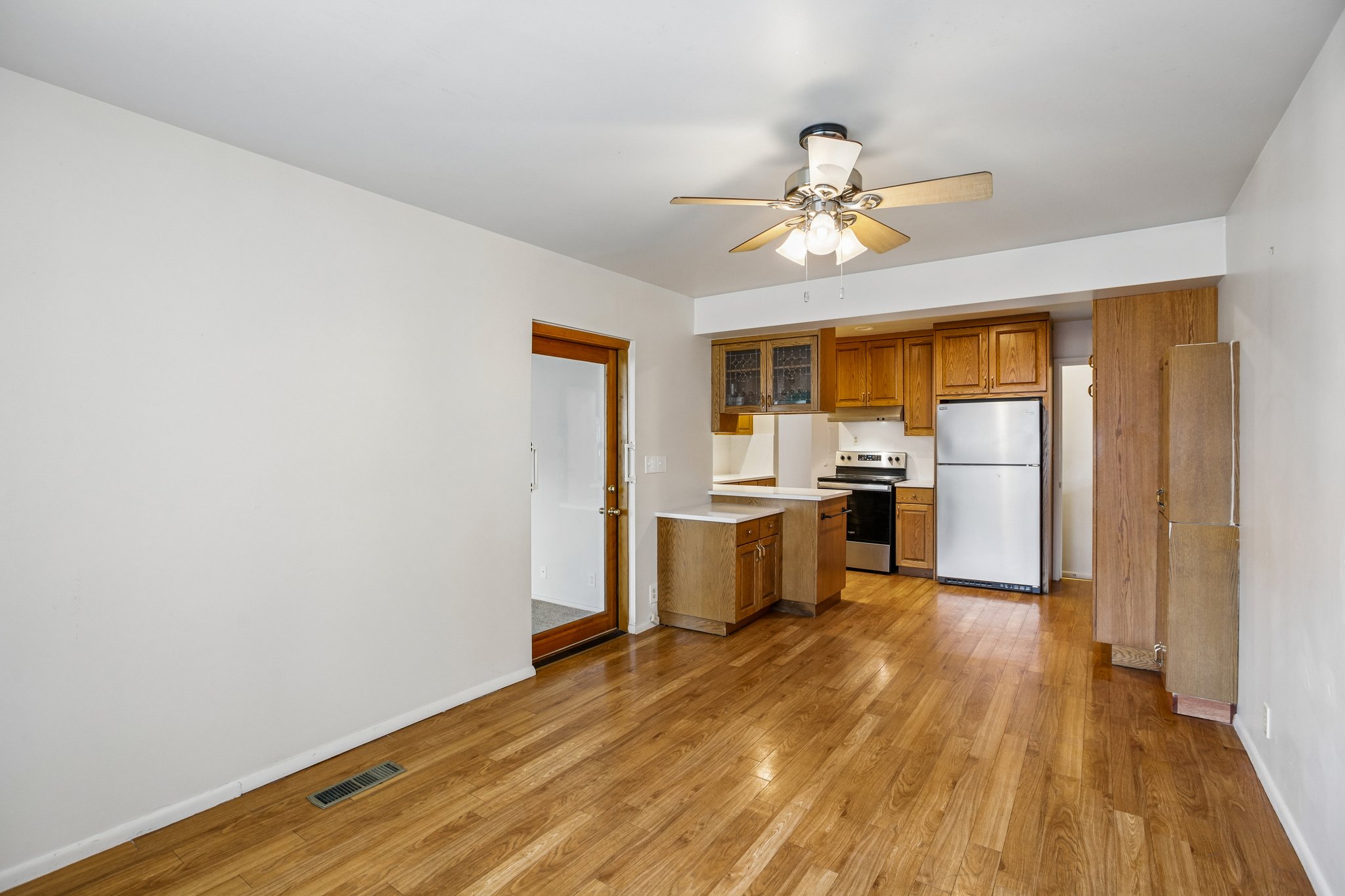Open-concept living space featuring wood-finish flooring, a ceiling fan with integrated lighting, and a kitchen area