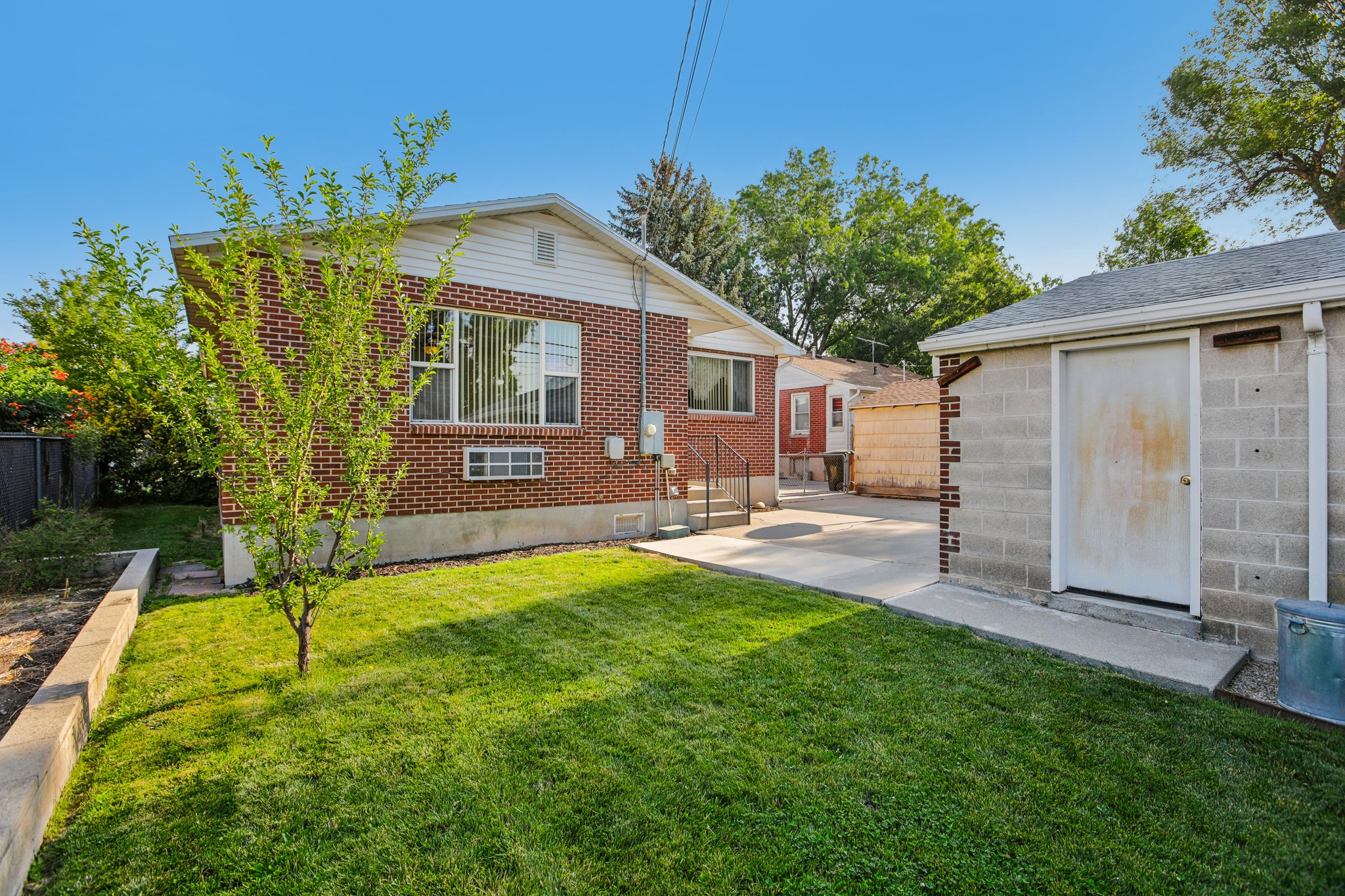 Spacious backyard featuring a manicured lawn, concrete patio, and a cinder block storage shed