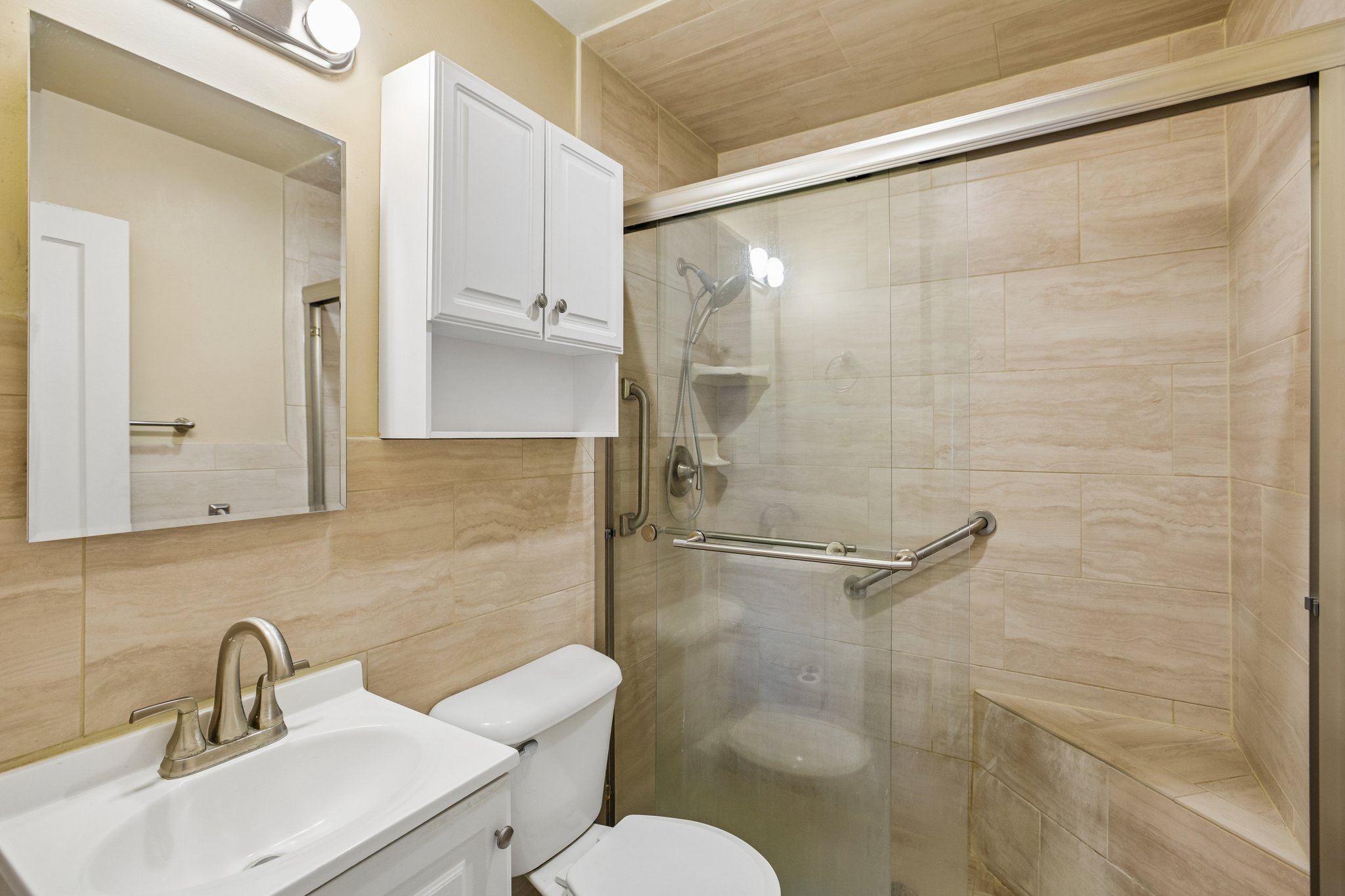 Bathroom with a glass-enclosed shower featuring a built-in bench, grab bars, and light-toned tilework