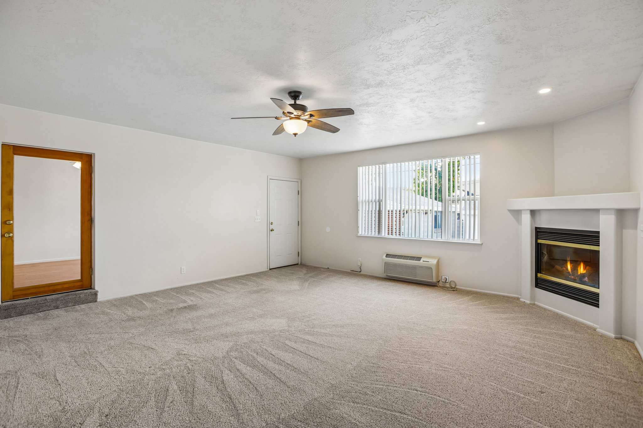 Spacious room featuring neutral carpeting, a ceiling fan with integrated lighting, recessed lighting, and a corner fireplace with a white mantel