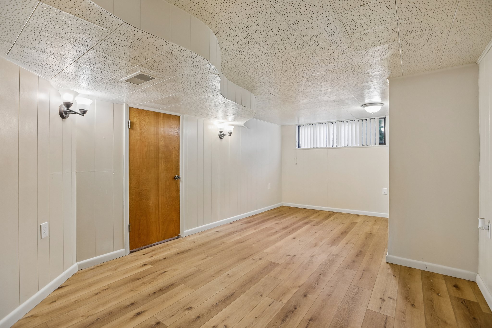 Finished room featuring wood-finish flooring, white paneled walls, and a textured drop ceiling