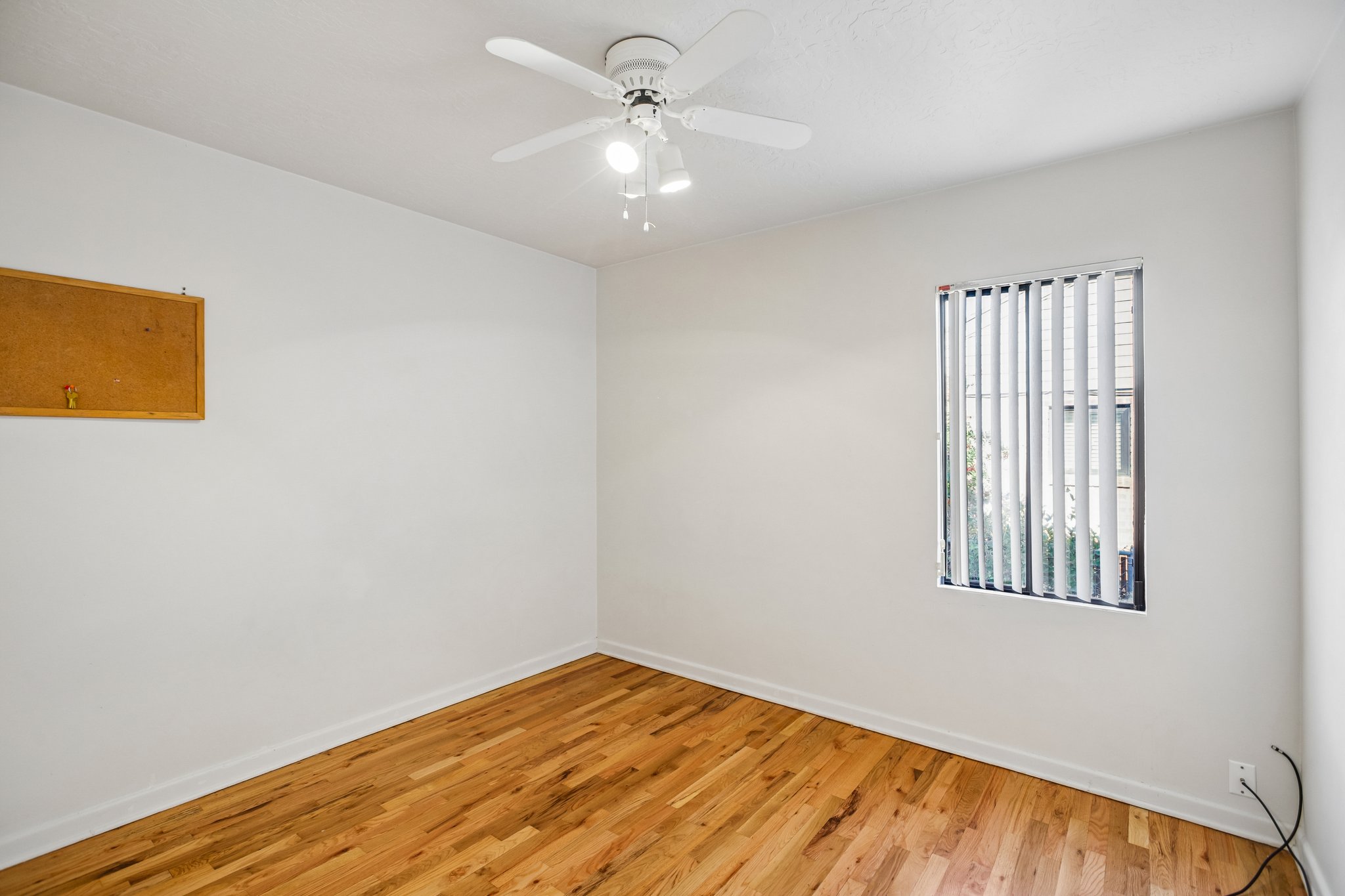 Room featuring wood-finish flooring, a ceiling fan with integrated lighting, and a single window with vertical blinds
