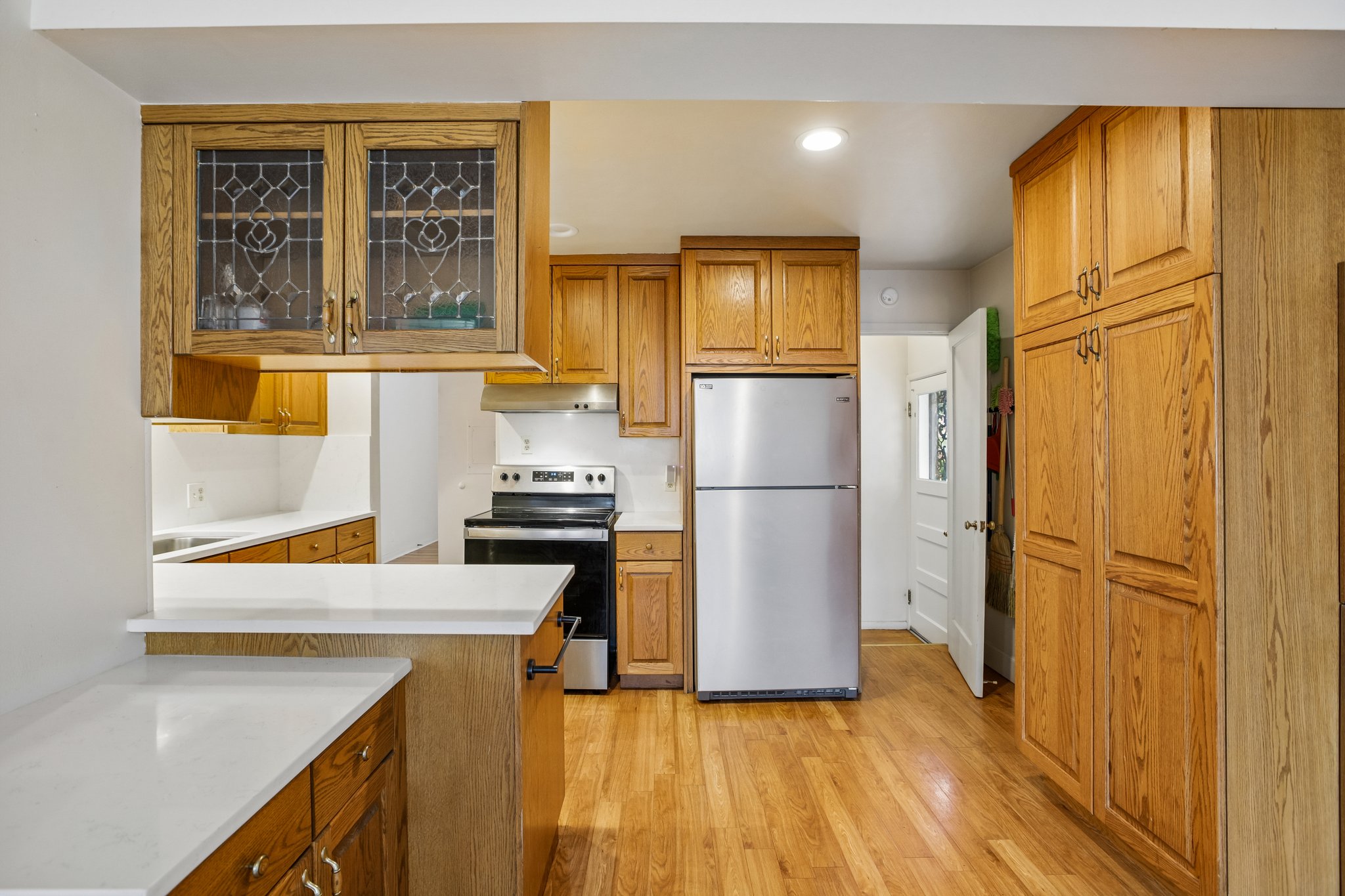 Kitchen featuring wood cabinetry, white countertops, stainless steel refrigerator, black range, and wood-finish flooring