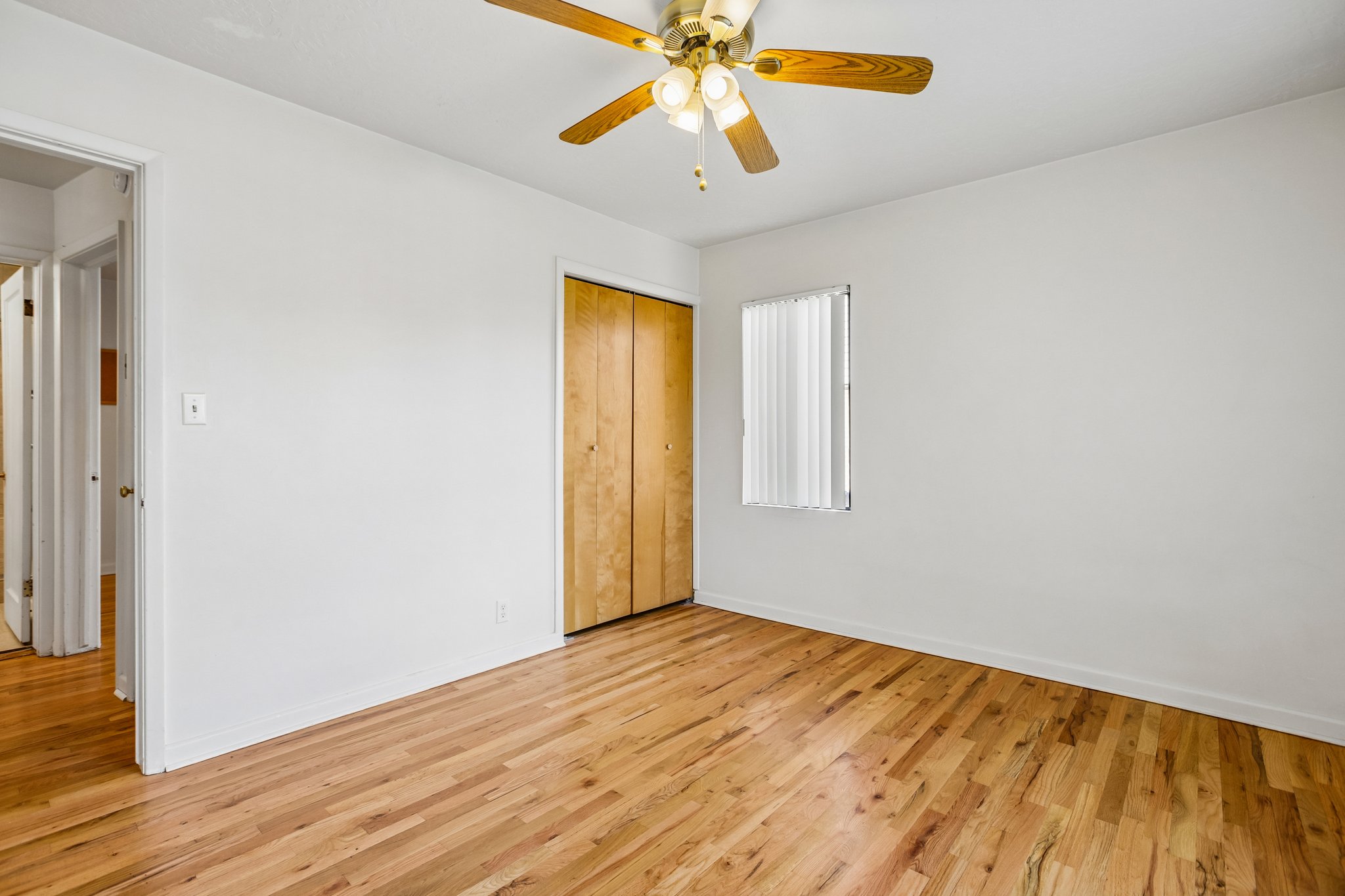 Room featuring wood-finish flooring, a ceiling fan with integrated lighting, a window with vertical blinds, and a bi-fold closet door