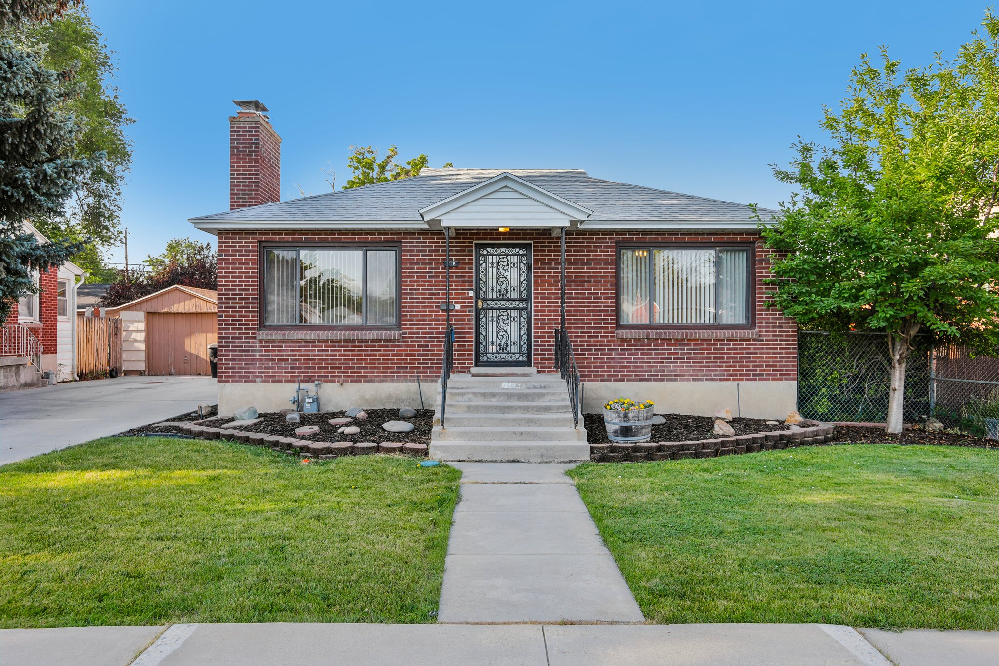 Brick exterior home featuring a concrete walkway, established front lawn, and foundational landscaping with decorative rocks