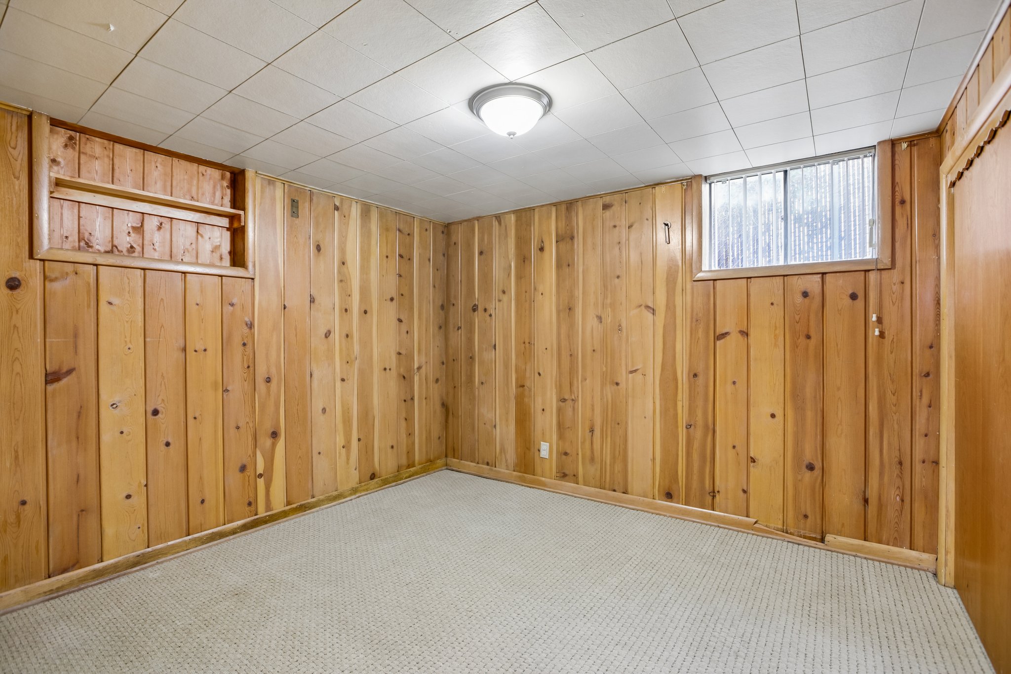 Room featuring wood paneling, drop ceiling, recessed window, and light-colored carpeting