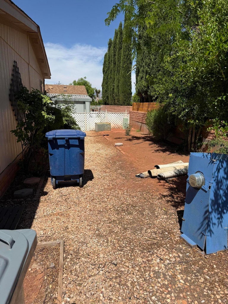 Gravel-covered side yard featuring a white lattice fence, mature trees, and a brick-capped privacy wall