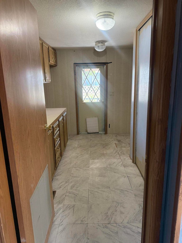 Hallway featuring wood-finish cabinetry, light-toned countertops, and a patterned tile floor
