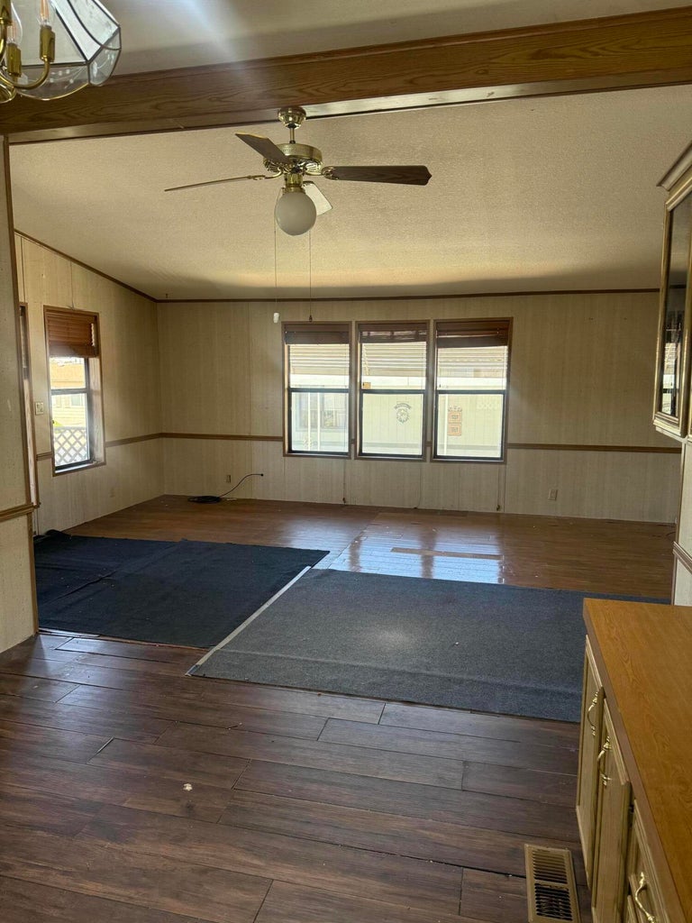 Spacious interior room featuring wood-finish flooring, a ceiling fan with light fixture, and a three-pane window configuration