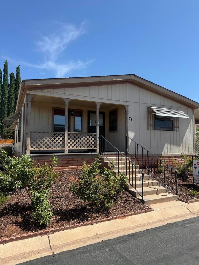 Single-story residence featuring light-colored siding, a covered front porch with lattice railing, and concrete steps with black metal handrails