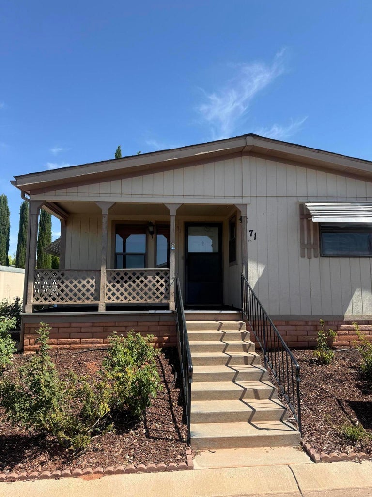 Front exterior featuring a covered porch, concrete steps with black metal railings, a dark entry door, and a light-colored siding facade
