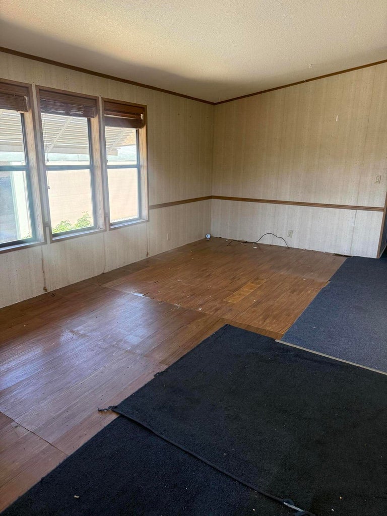Room featuring three windows, wood-finish flooring, and partial wall paneling