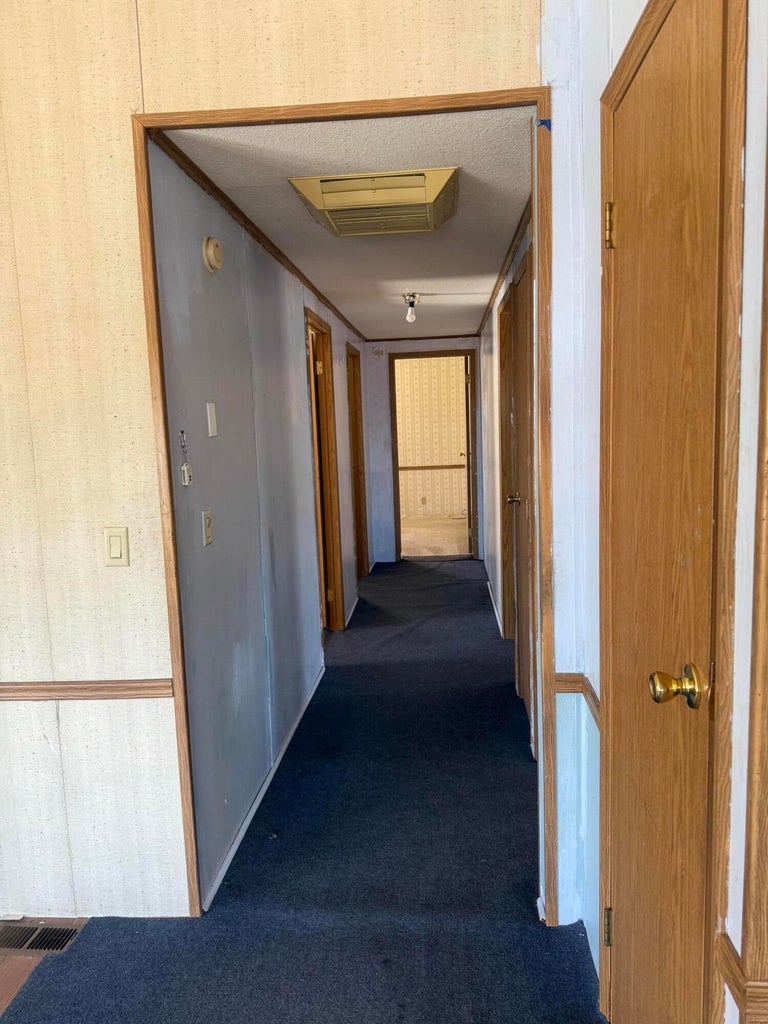 Hallway with wood-finish doors, dark carpet flooring, and integrated lighting fixtures