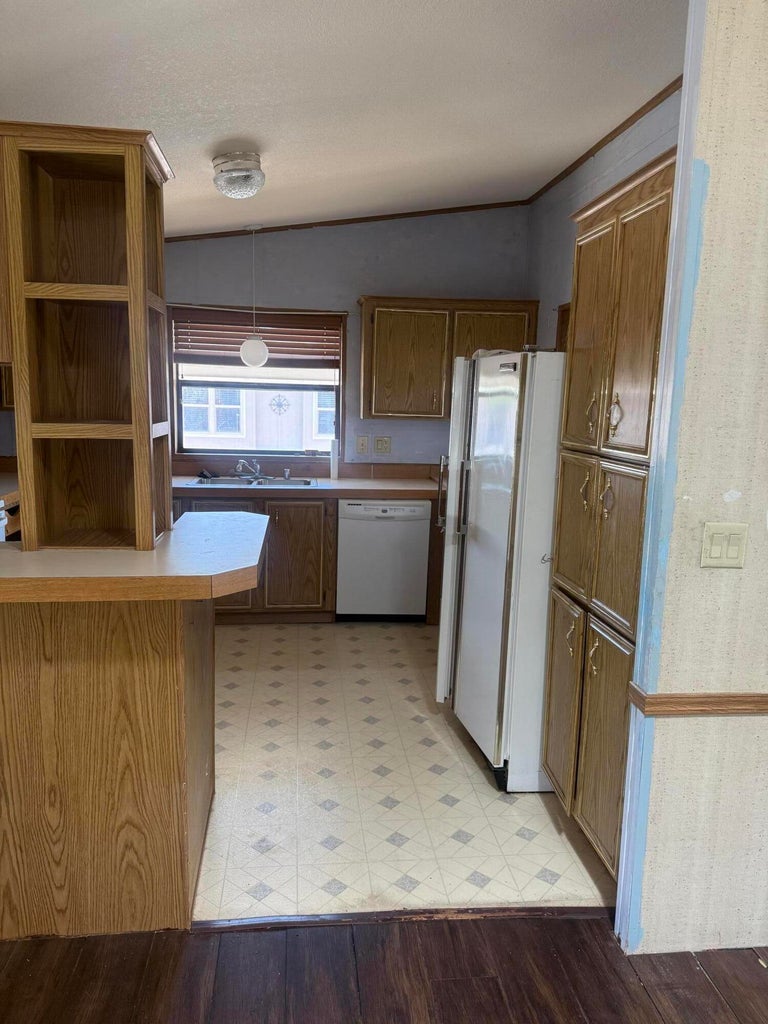 Kitchen featuring wood-finish cabinetry, a white refrigerator, a white dishwasher, and a double basin sink beneath a window
