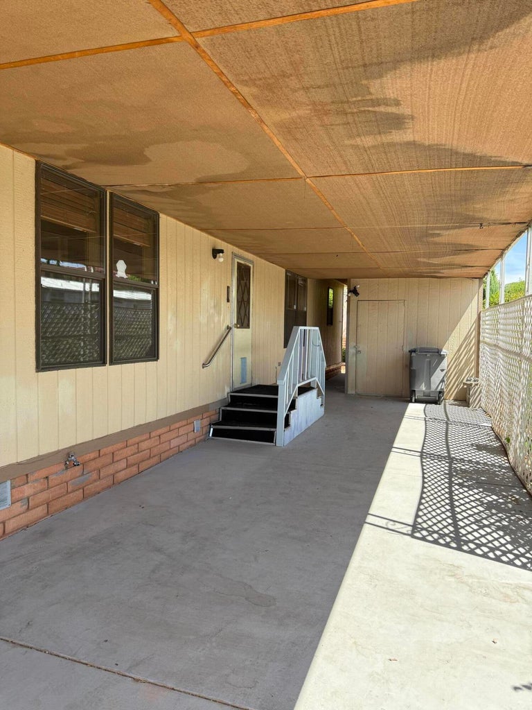 Covered concrete carport with a beige paneled exterior and a brick-finish base