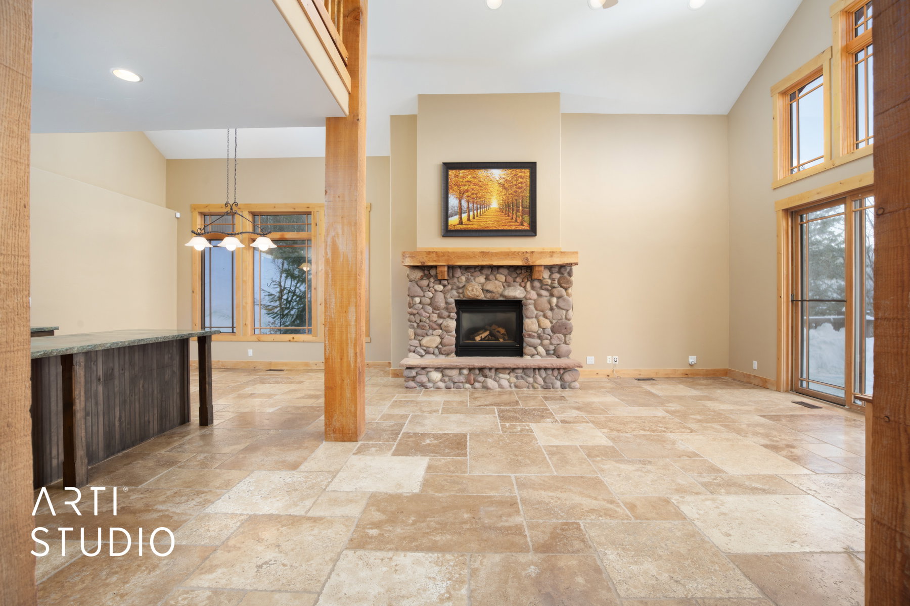 Spacious living area featuring a river stone fireplace with a wood mantle, vaulted ceilings, and large format tile flooring