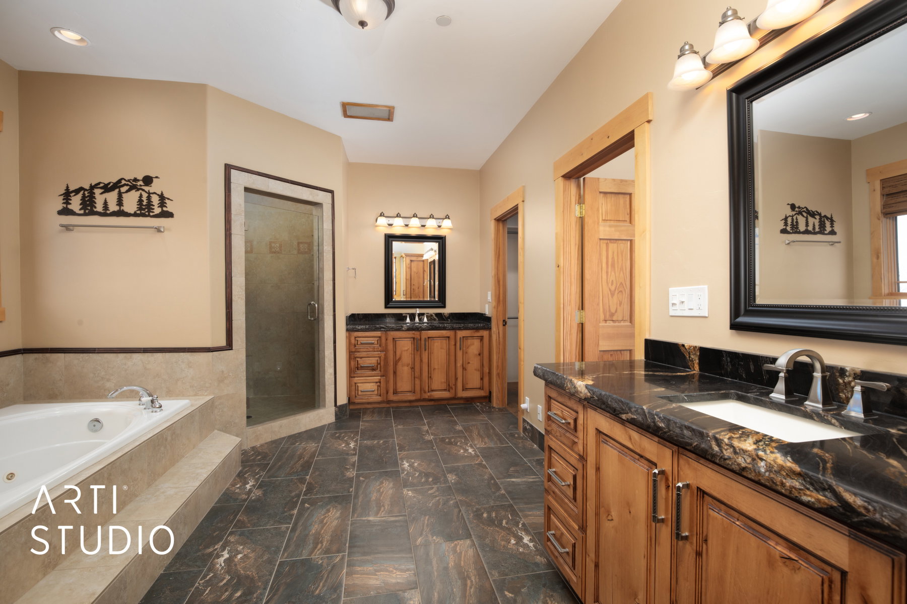Spacious bathroom featuring a built-in jetted tub, a separate glass-enclosed shower, dual vanities with integrated sinks, and dark stone countertops