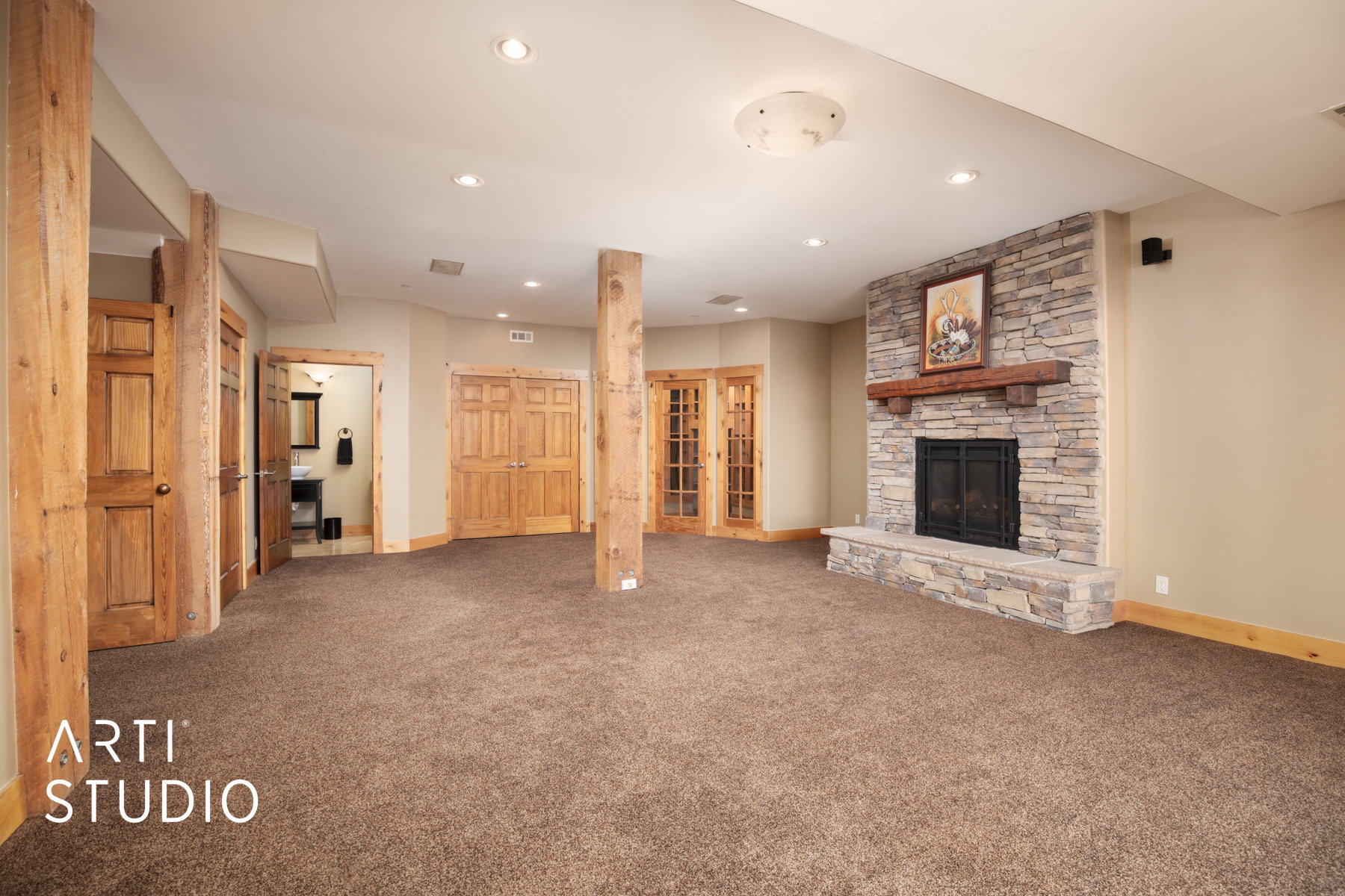 Spacious room featuring a stone-faced fireplace with a wood mantle, recessed lighting, wood-finish columns, and warm neutral carpeting