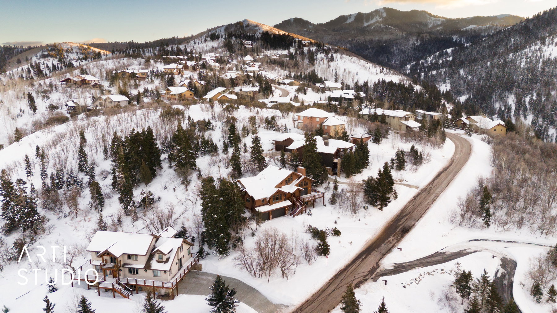 Mountainous terrain featuring snow-covered slopes, evergreen trees, and a winding paved road
