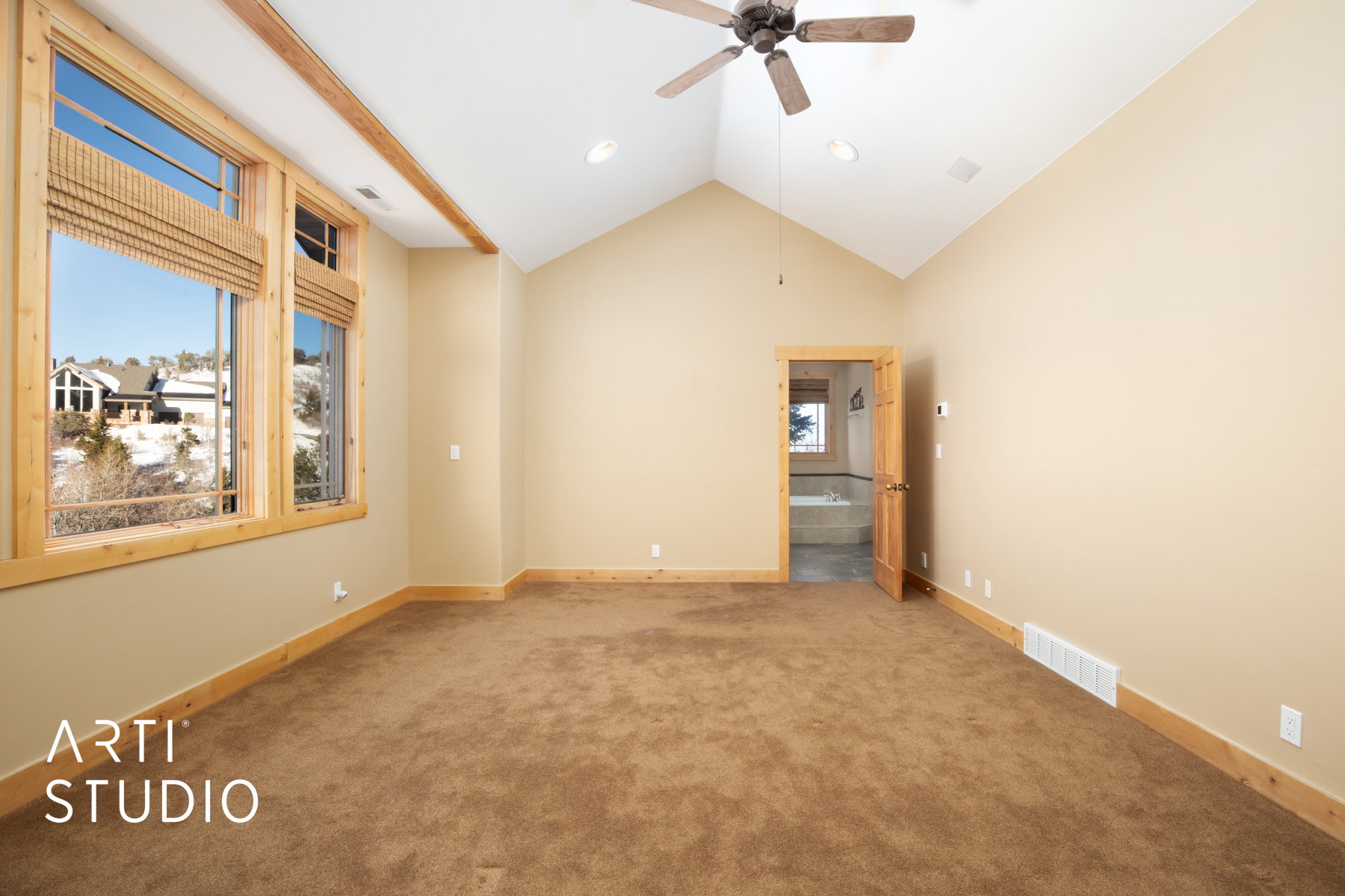 Spacious carpeted room featuring a vaulted ceiling and a wood-finish ceiling fan