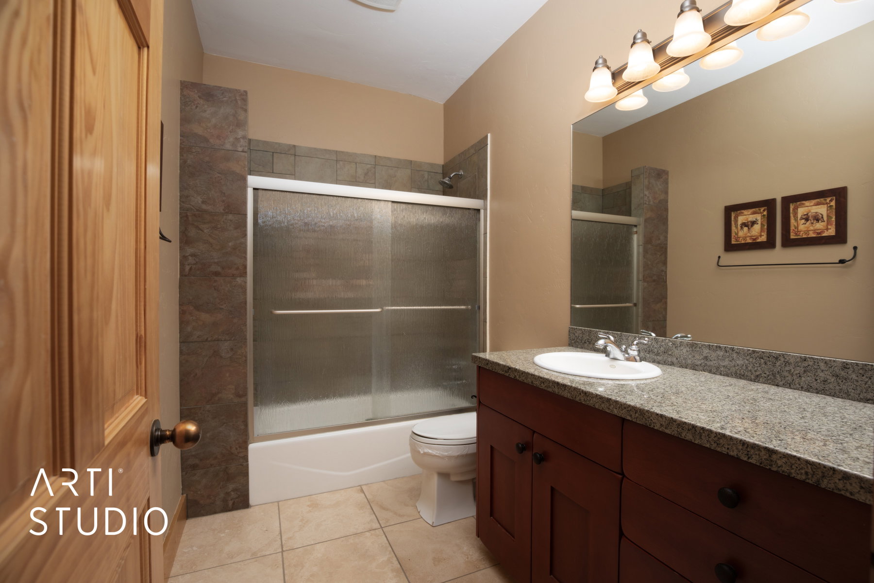 Bathroom featuring a wood-panel door, floor-to-ceiling tiled shower with sliding glass doors, a vanity with a light-colored countertop, and a large mirror with overhead lighting