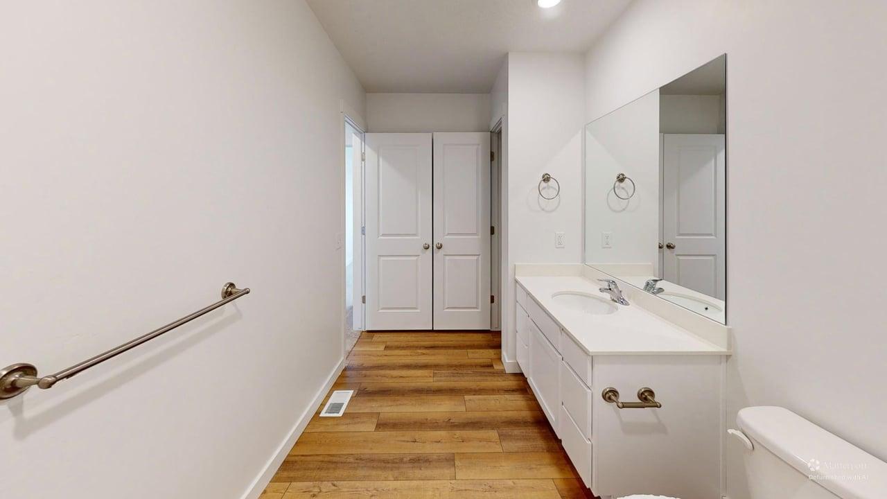 Contemporary bathroom featuring a long single vanity with an integrated sink, a large mirror, dual closet doors, wood-finish flooring, and recessed lighting