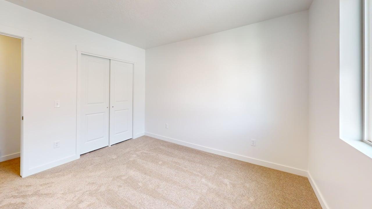 Bright interior space featuring neutral carpeting, white walls, white trim, a double sliding closet door, and a large window