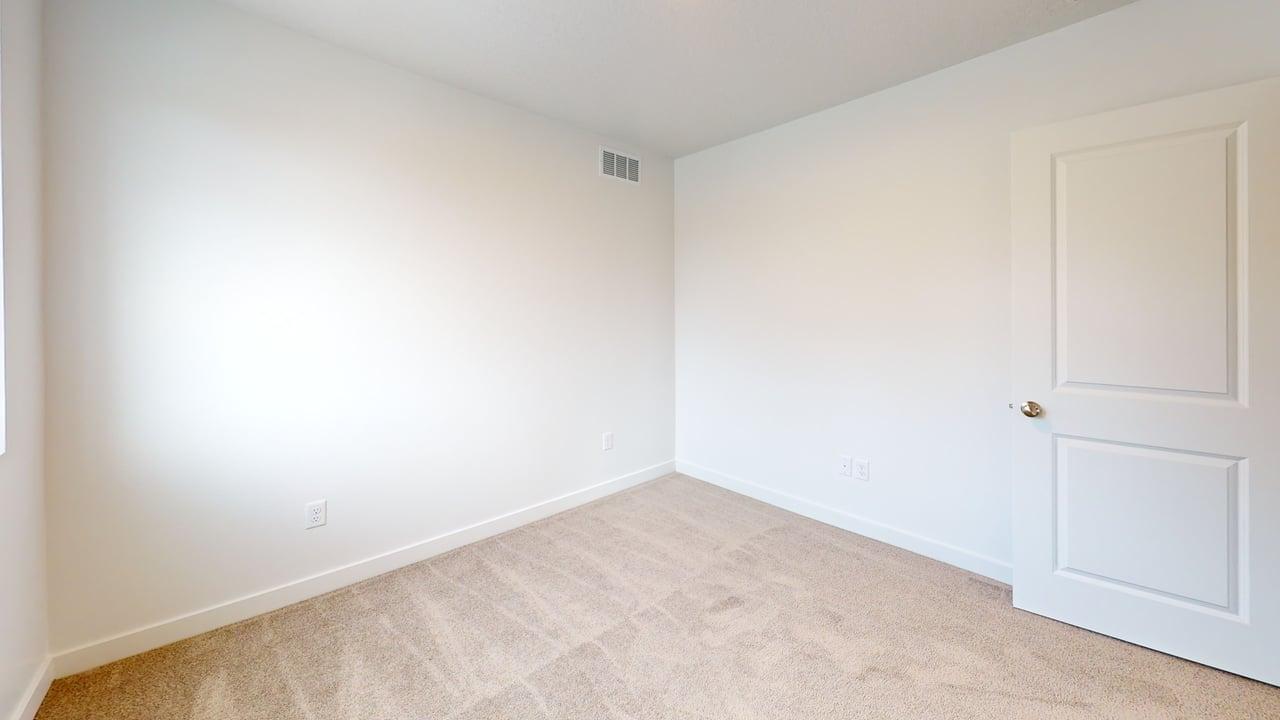 Room featuring neutral-toned walls, plush carpeting, a white paneled door with a brass-toned doorknob, white baseboards, and a visible air vent