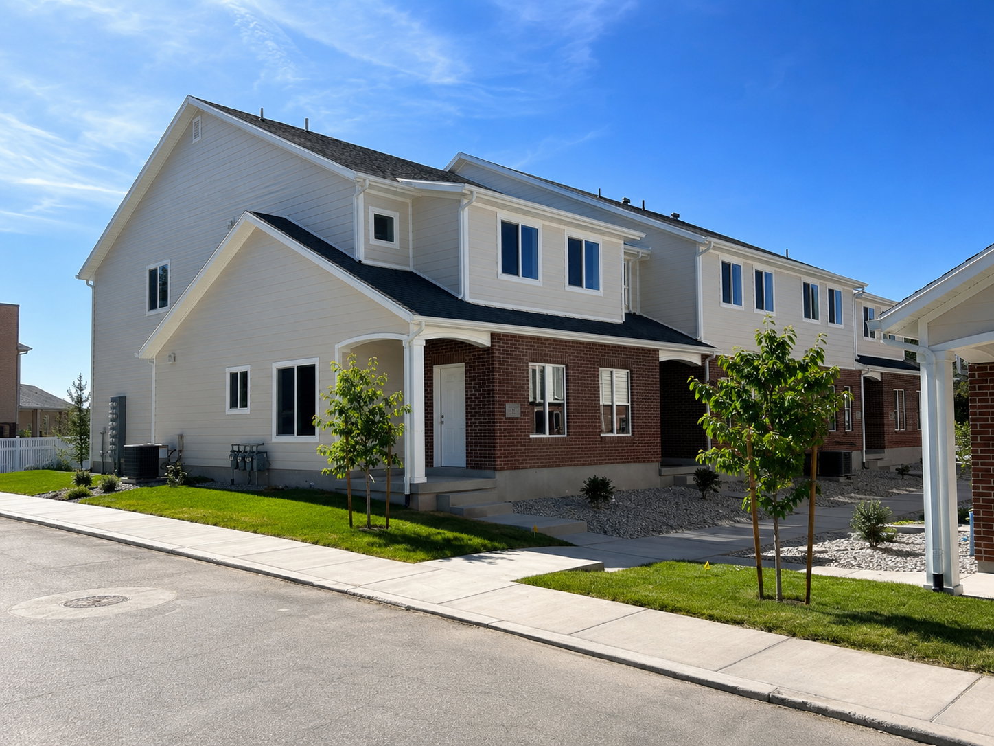 Contemporary townhome exterior featuring brick and light-toned siding, a covered entry, established sidewalks, and newly planted landscaping