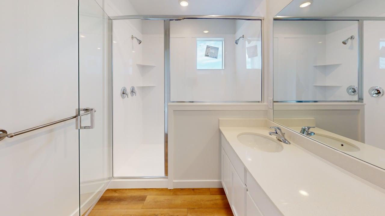 Modern bathroom featuring a double vanity with integrated sinks, a large mirror, and a glass-enclosed shower with a grab bar and built-in shelving