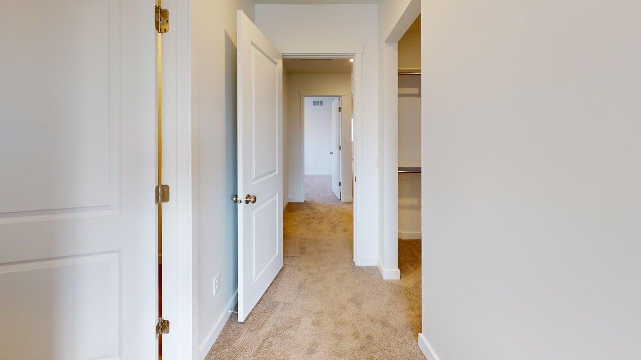 Hallway featuring neutral-toned carpeting, white interior doors with gold-tone hardware, and a closet with shelving and hanging rods