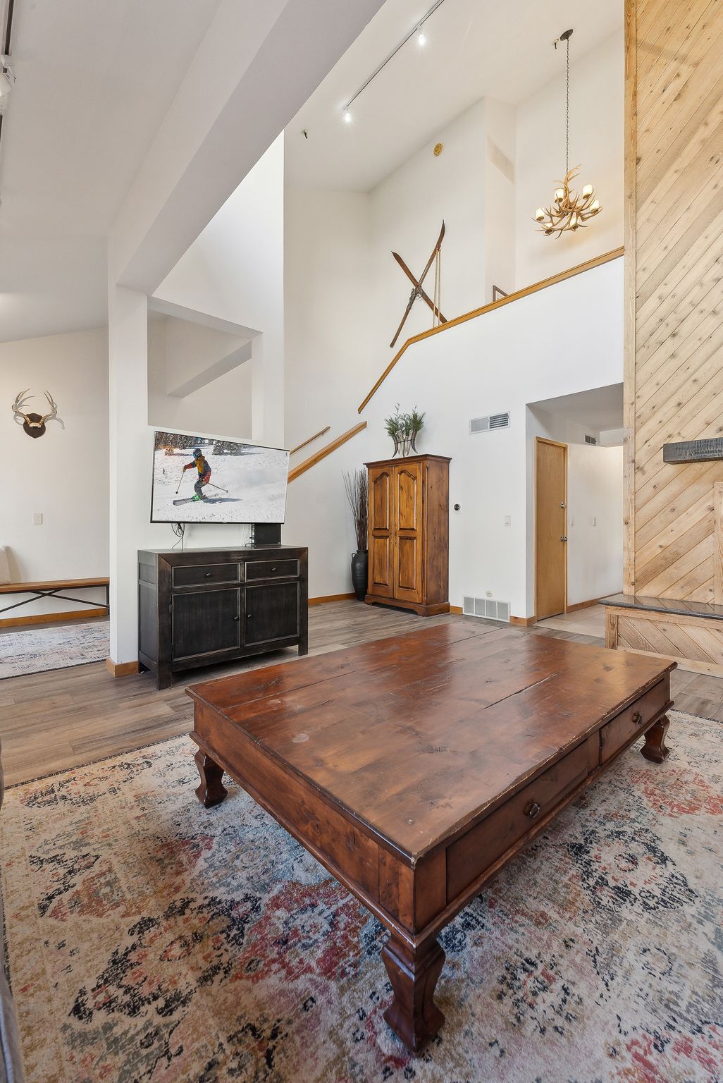 Living area featuring vaulted ceilings, wood-finish flooring, a wood accent wall, and an upper-level balcony
