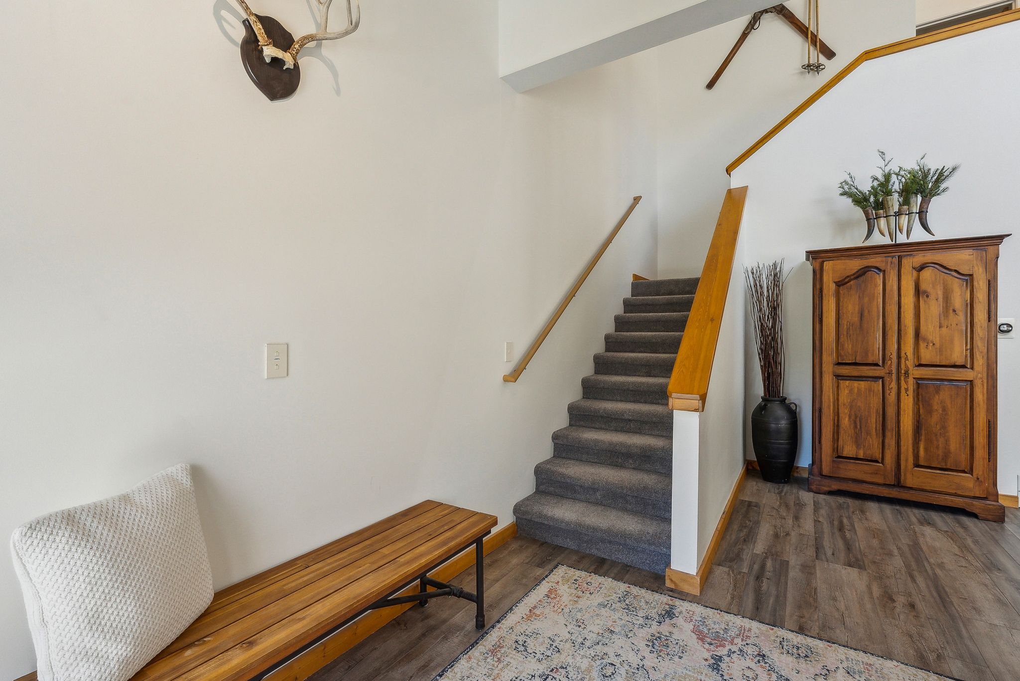 Carpeted staircase with wood handrail, wood-finish flooring, and white walls