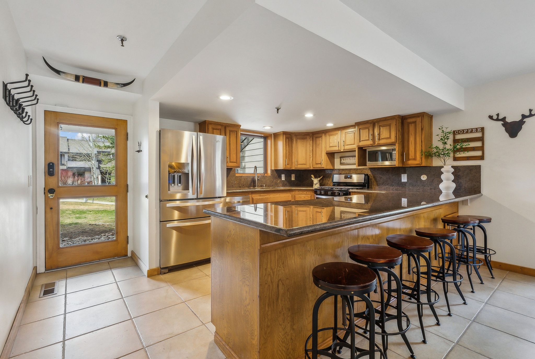 Kitchen featuring wood cabinetry, stainless steel appliances, dark stone countertops, and a peninsula with bar seating