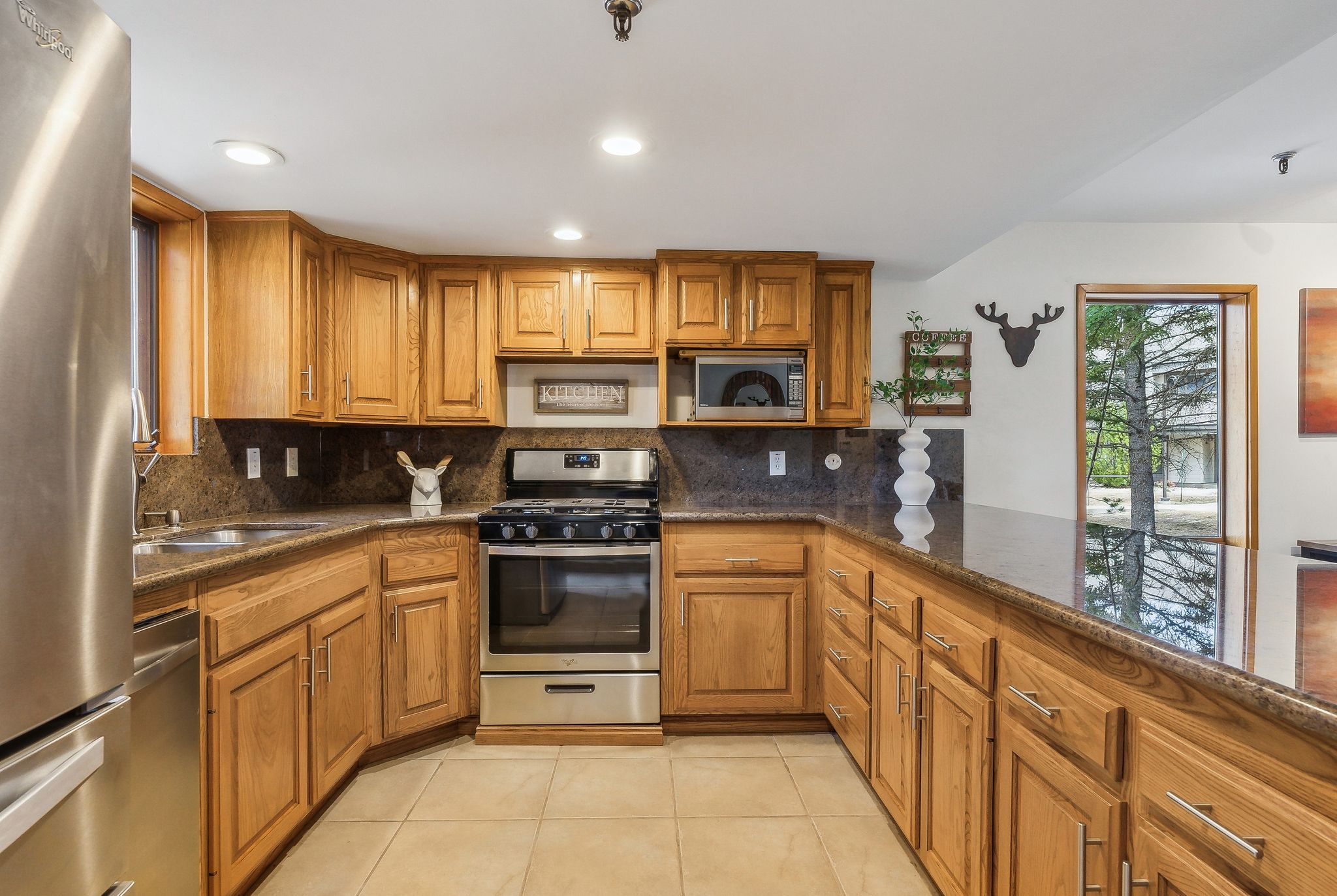 Kitchen featuring wood cabinetry, dark stone countertops, stainless steel appliances, and tile flooring