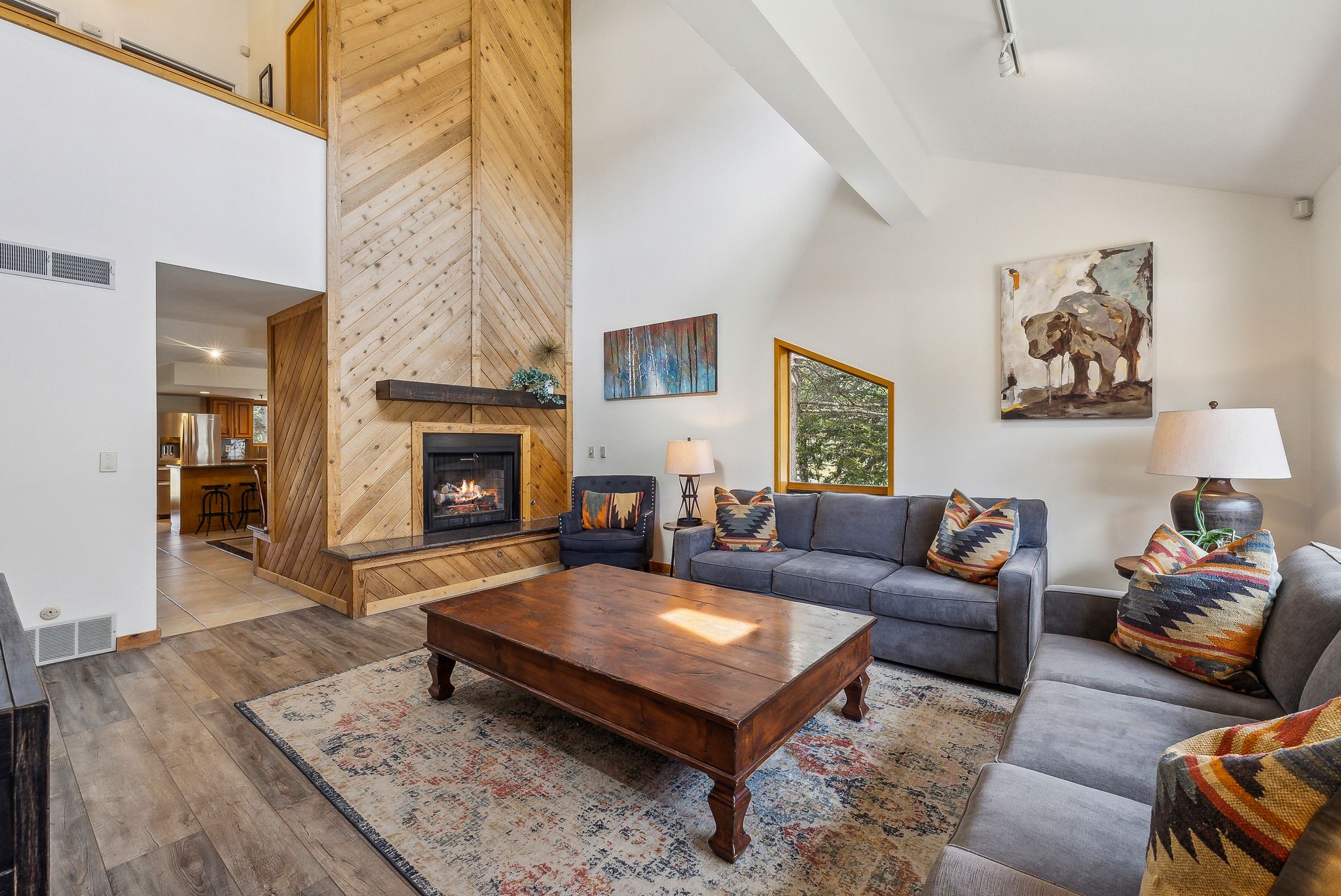 Living area featuring a floor-to-ceiling wood-paneled fireplace with a dark wood mantel, vaulted ceilings, and wood-finish flooring